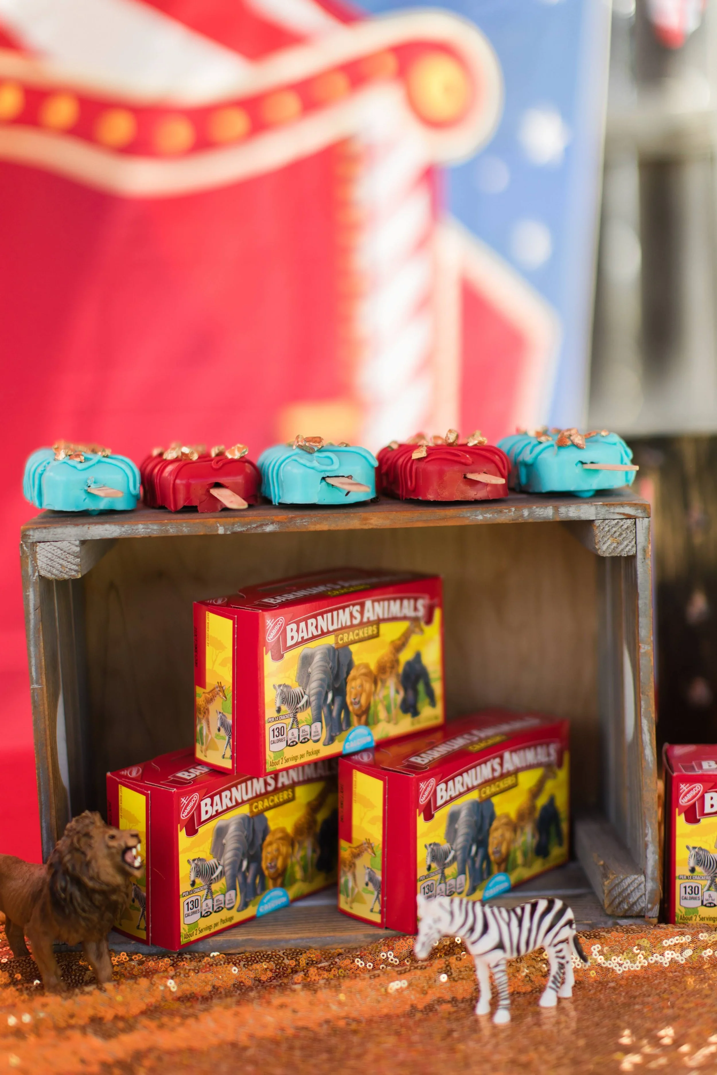 Miniature animal figures in front of a display of Buffalo chicken wing dipped chocolates and a box of Barnum's Animals animal crackers.