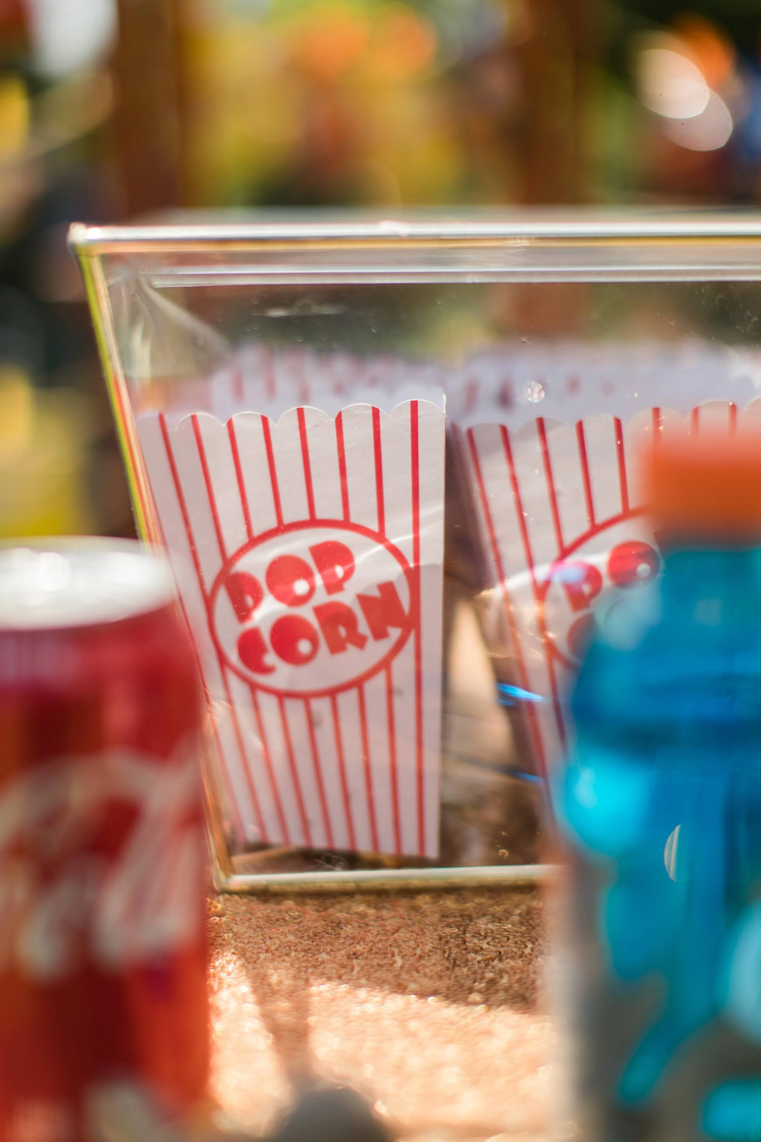 A clear container holding popcorn bags with red and white stripes and the words 'POP CORN' in red.