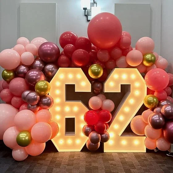 Decorative balloon arrangement with pink, purple, red, and gold balloons surrounding illuminated numbers 92.