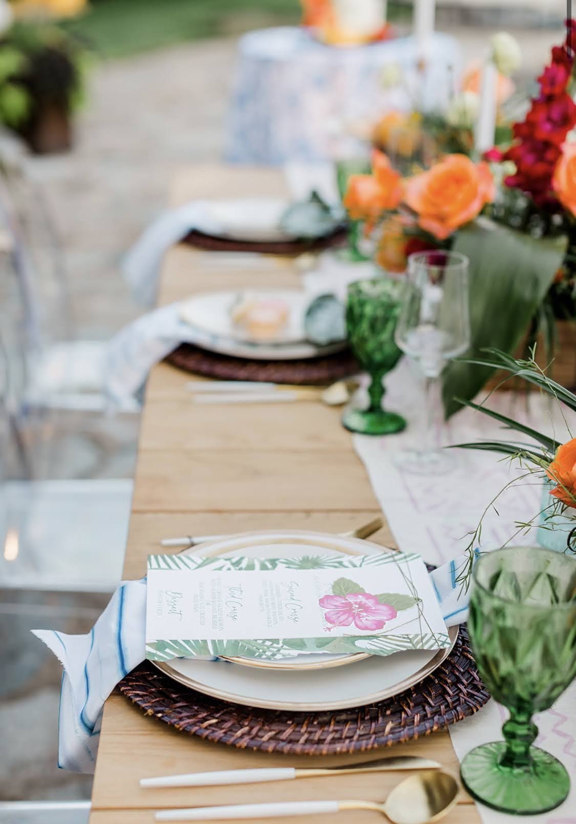 Decorated outdoor dining table with plates, glasses, silverware, floral arrangements, and menus