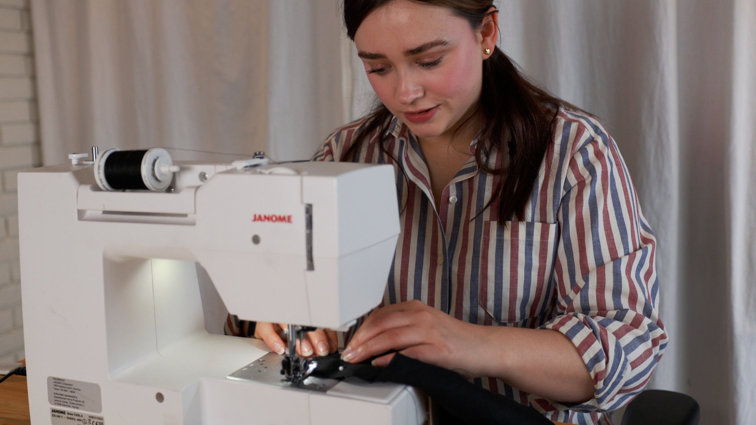 A woman working on a sewing machine, wearing a striped shirt, with a focused expression.