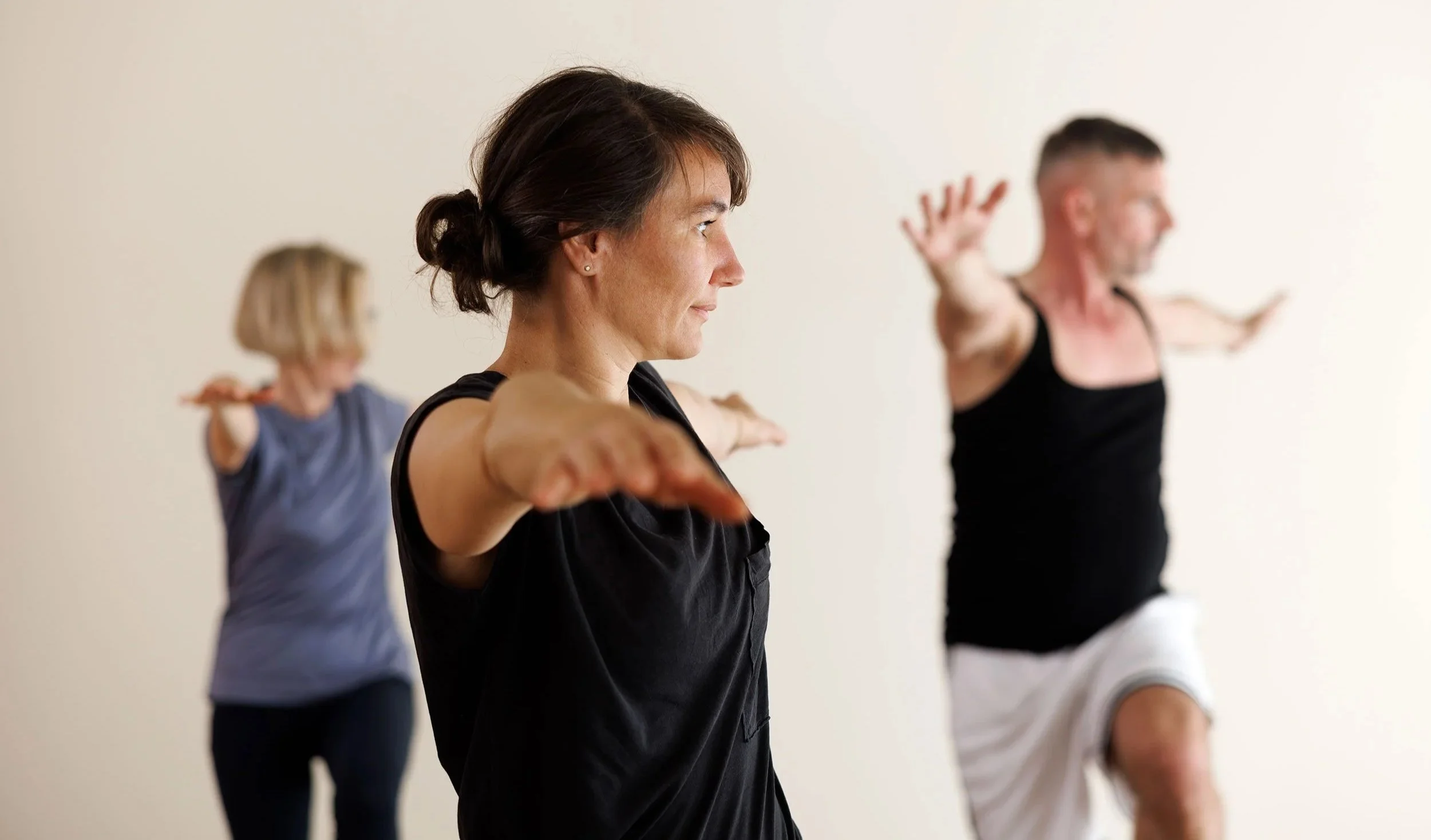 Drei Menschen machen Yoga-Übungen in einem Yoga Sudio. Die Frauen sind in der Mitte und auf der linken Seite und der Mann ist auf der rechten Seite.