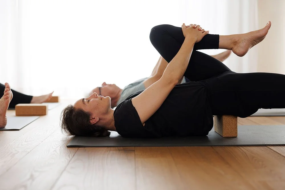 Menschen machen Yoga auf Matten auf einem Holzfussboden, unterstützen sich gegenseitig bei einer Übung.