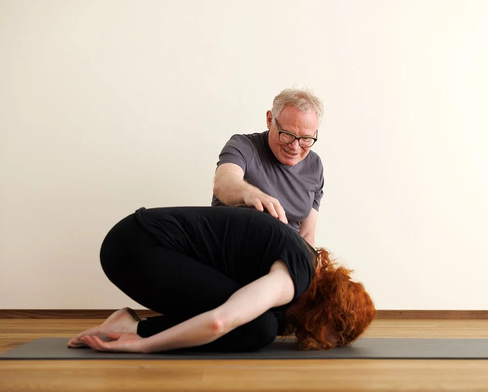 Frau macht Yoga im Yoga-Studio auf einer Yogamatte, sitzend mit einem Bein ausgestreckt und das andere Knie angezogen, hält ihre Knie umarmt und schaut nach unten.