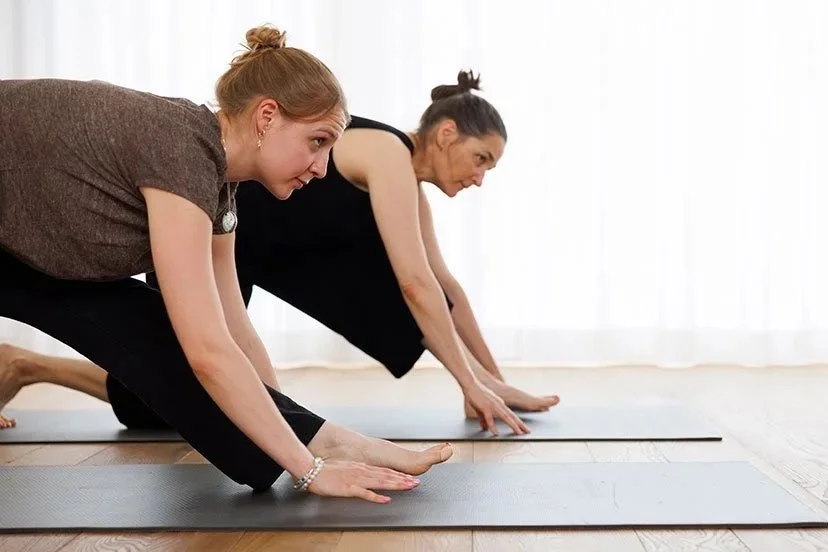 Menschen beim Yoga im Fitnessraum, beide in Cobra-Position auf Yogamatten, mit großen Fenstern und weißen Wänden im Hintergrund.