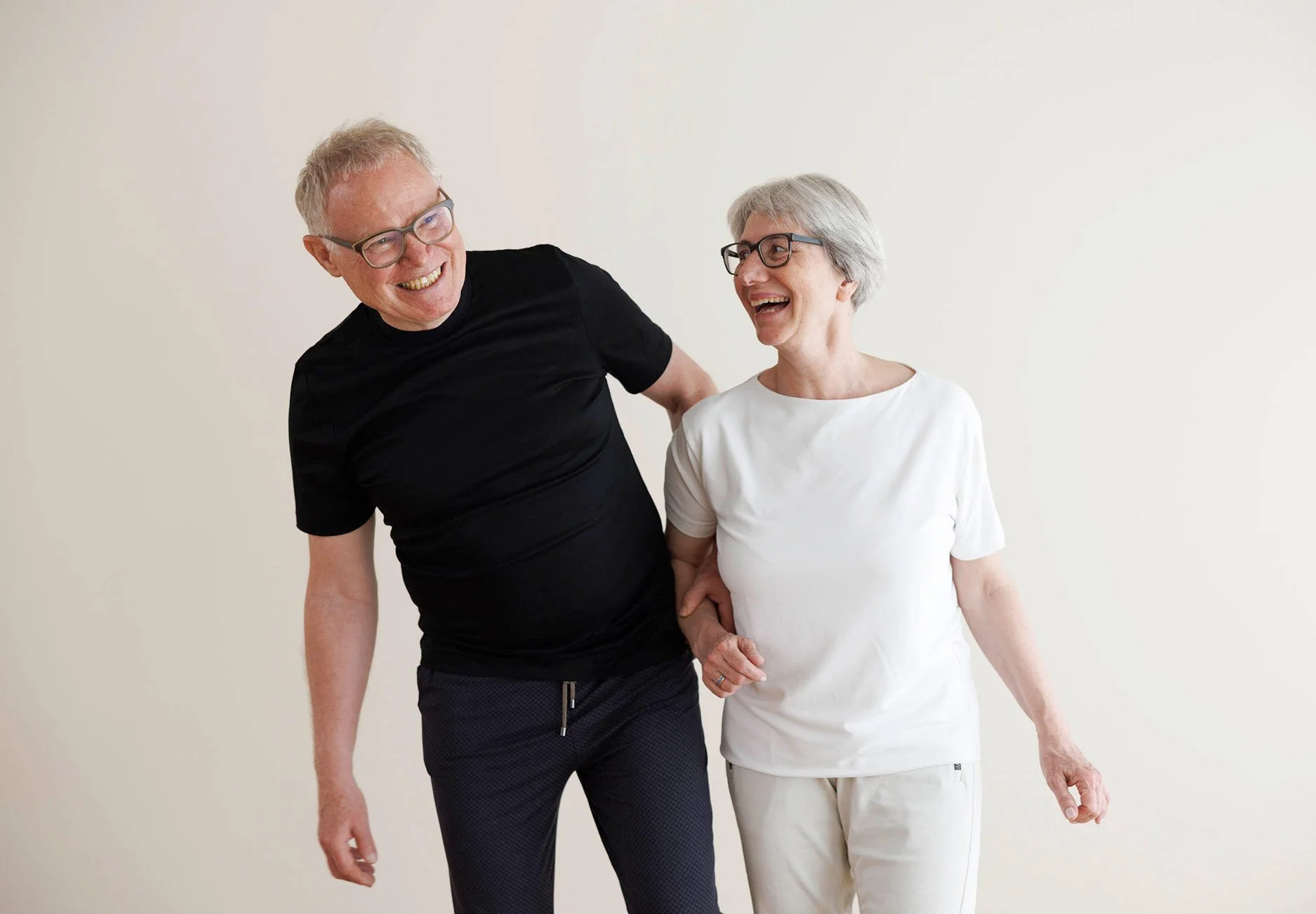 Ein Mann und eine Frau lachen zusammen, während sie Händchen halten, vor einem weißen Hintergrund.