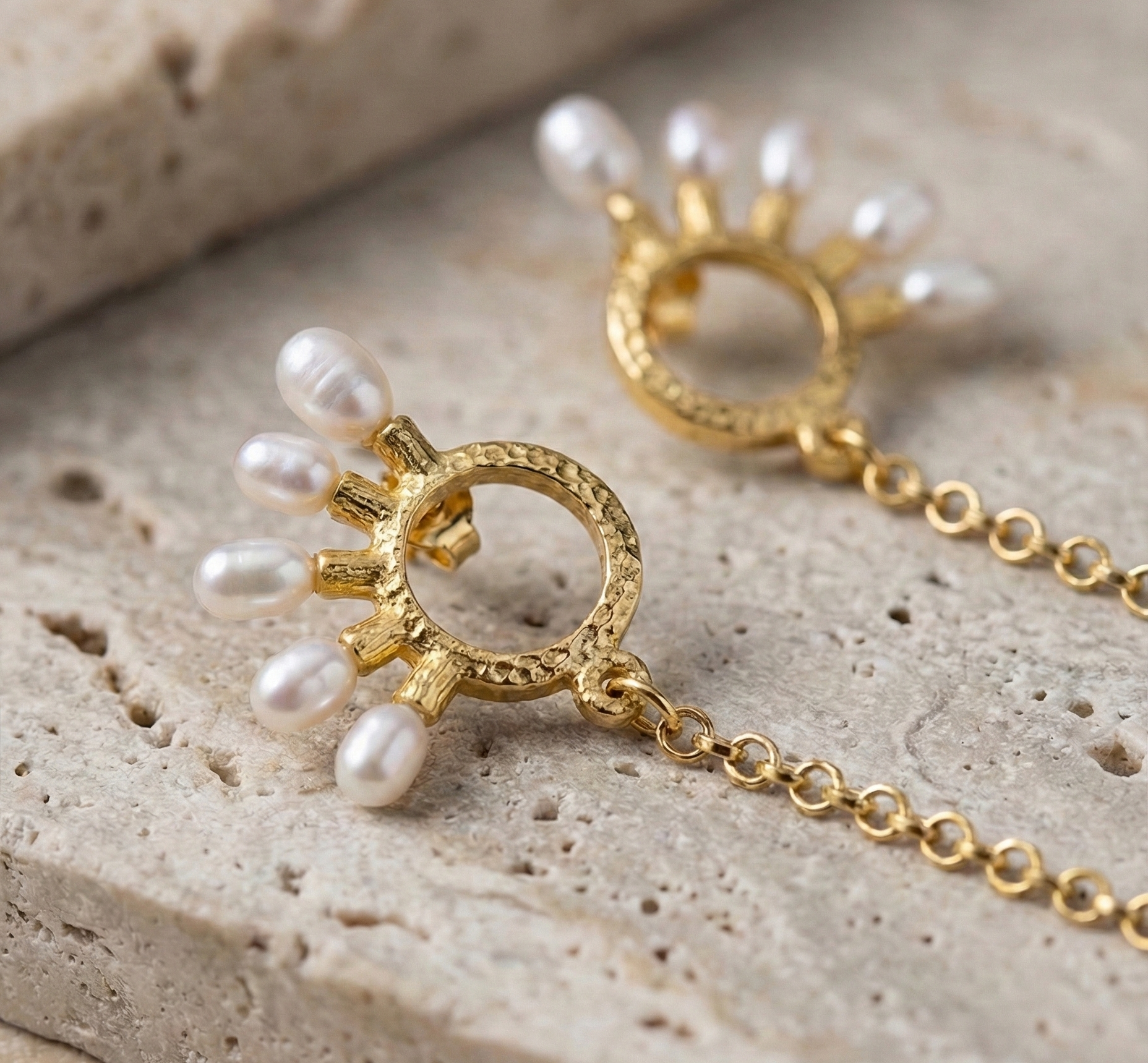 A pair of gold-plated earrings decorated with pearls on a stone surface.