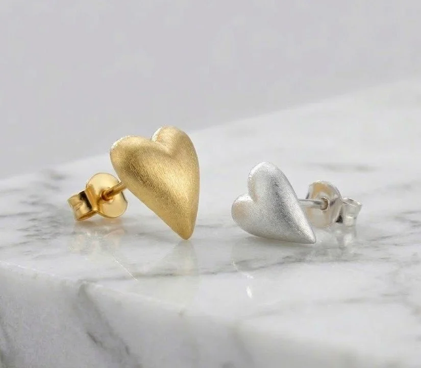 Gold-plated and sterling silver heart-shaped stud earrings on a marble surface.