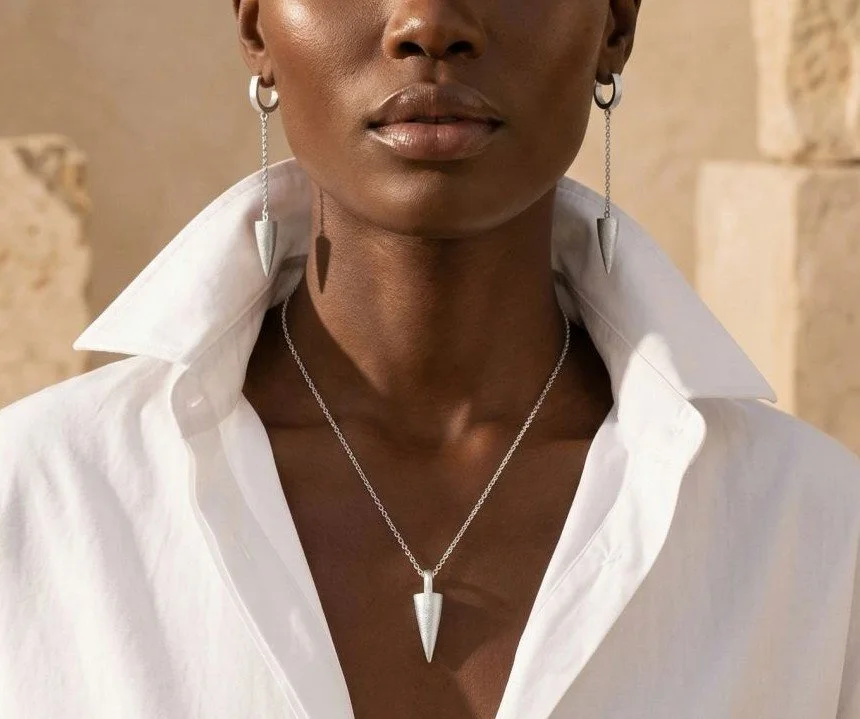 Close-up of a woman wearing sterling silver jewellery, including dangling earrings and a necklace with a spike pendant, dressed in a white shirt with an open collar.