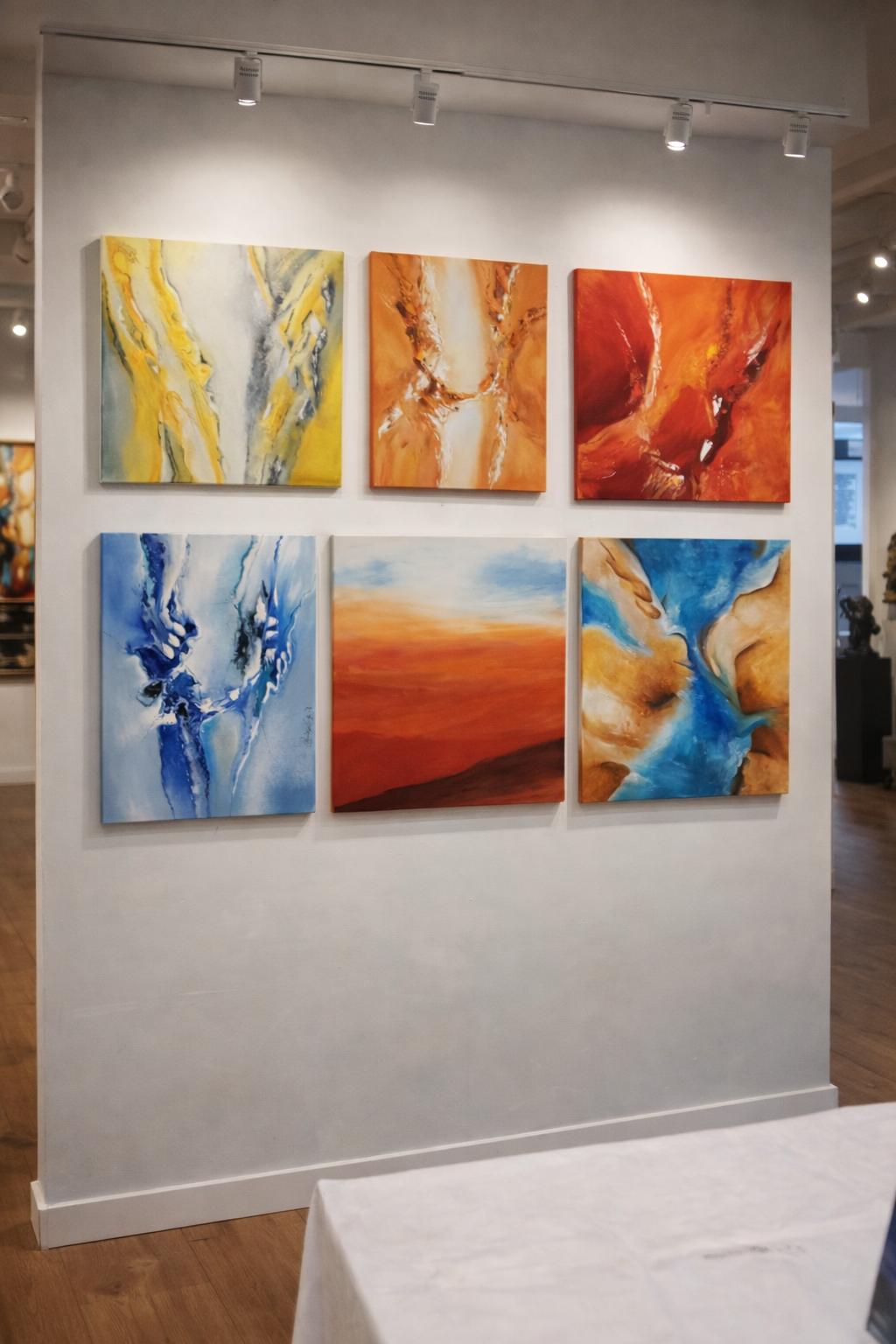 Sechs abstrakte Gemälde in lebendigen Farben auf einer weißen Wand in einer Galerie.