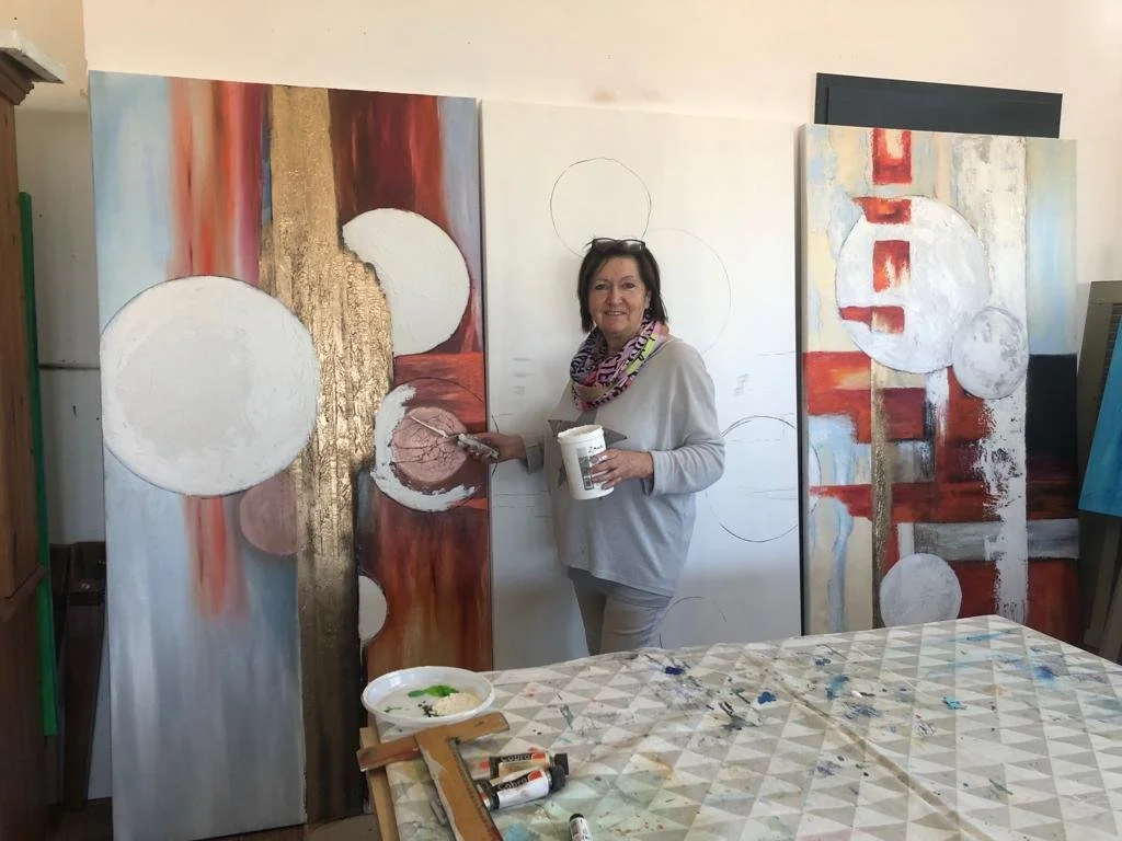 Frau beim Malen abstrakter Kunstwerke mit weißen Kreisen auf großen Leinwänden in einer Kunstwerkstatt.