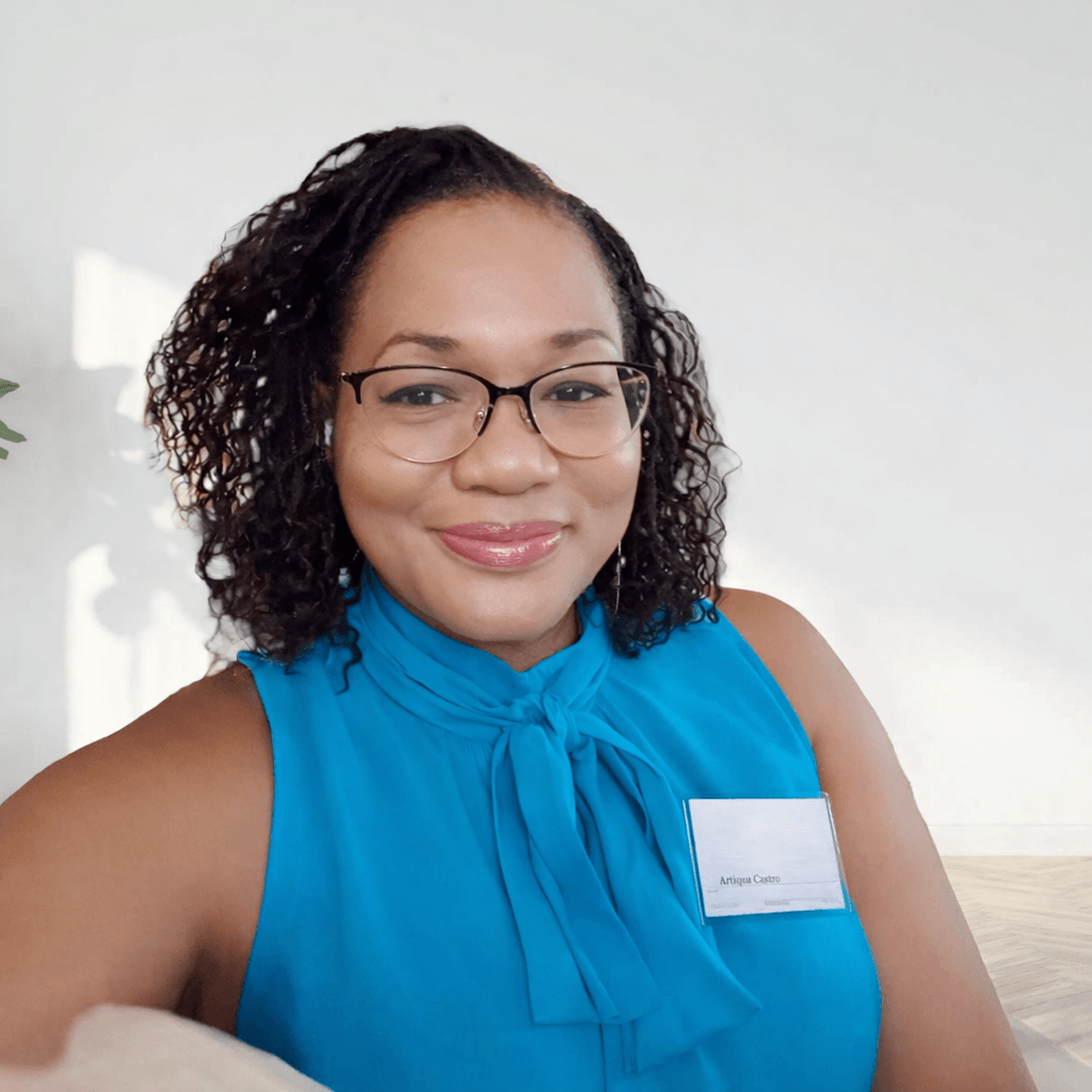 A woman wearing glasses and a bright blue sleeveless top with a bow is smiling at the camera.