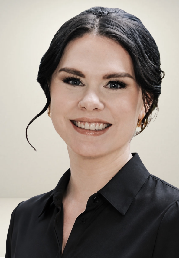 A woman smiling with dark hair styled in loose waves, wearing a black collared shirt and gold hoop earrings, against a plain off-white background.