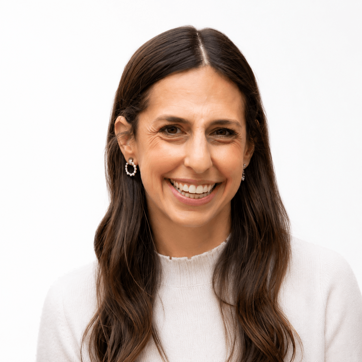 A woman with long brown hair, wearing a white sweater and pearl earrings, smiling against a plain white background.