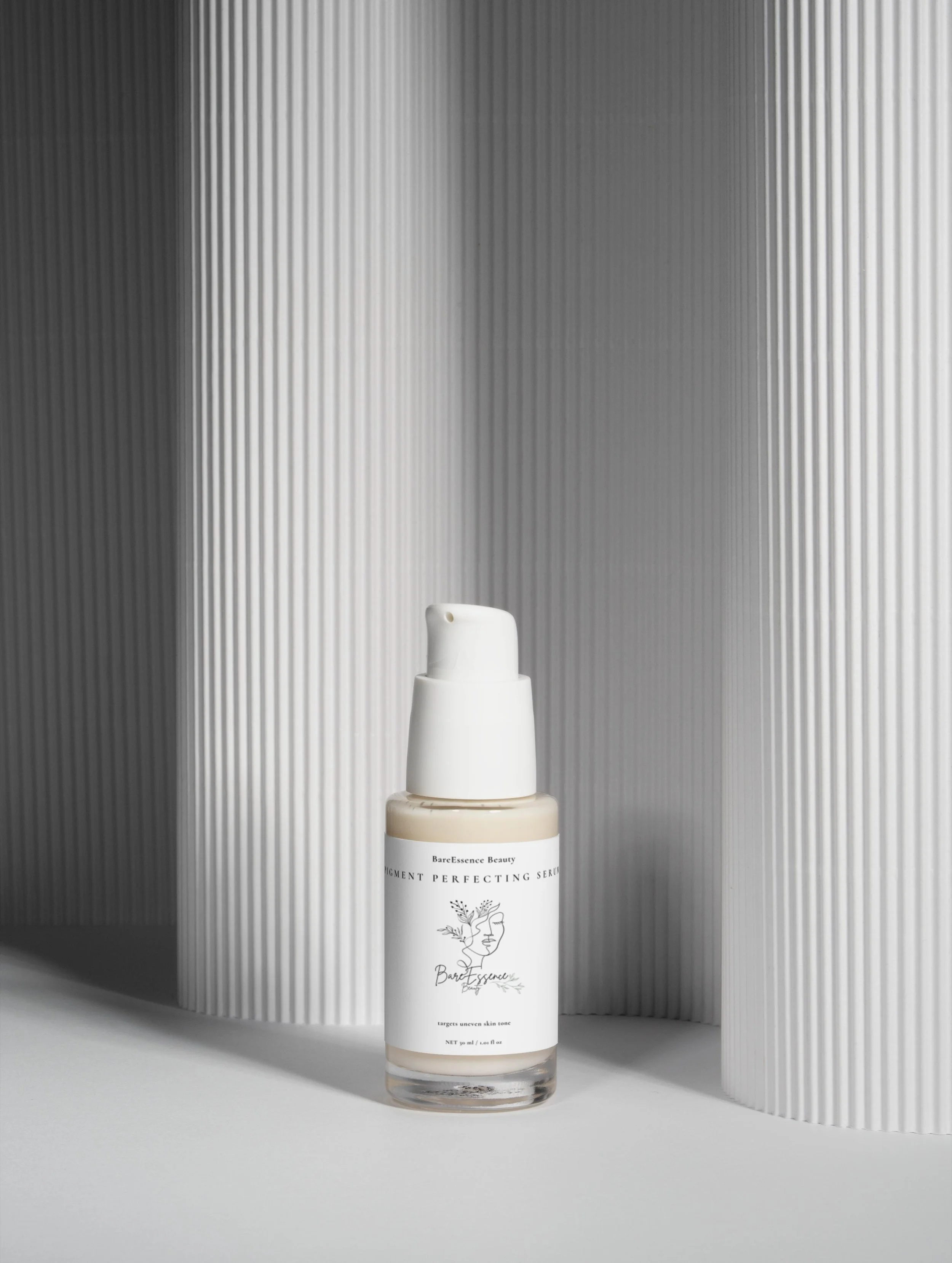 A bottle of BareEssence Beauty Pigment Perfecting Serum on a white surface, with a textured white and gray background.