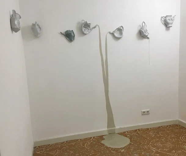 Danijela Pivašević-Tenner, Im Fluss – Kahla, 2016  7 teilige Wandarbeit Porzellan gegossen, deformiert und gebrannt bei 1320 Grad, Glasur transparent und Celadon  ca. 25 x 19 x 8 cm - Verformte Kaffeekannen an der Wand mit Porzellanstrahl