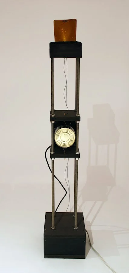 Strombetriebene kinetische Skulptur. Sie gleicht einem hoher Turm, dessen dünne Rohre der Konstruktion Leichtigkeit verleihen. Eine Dose in der Mitte leitet zufallsgetrieben Strom zu der Lampe an der Spitze, die Leuchtsignale sendet.