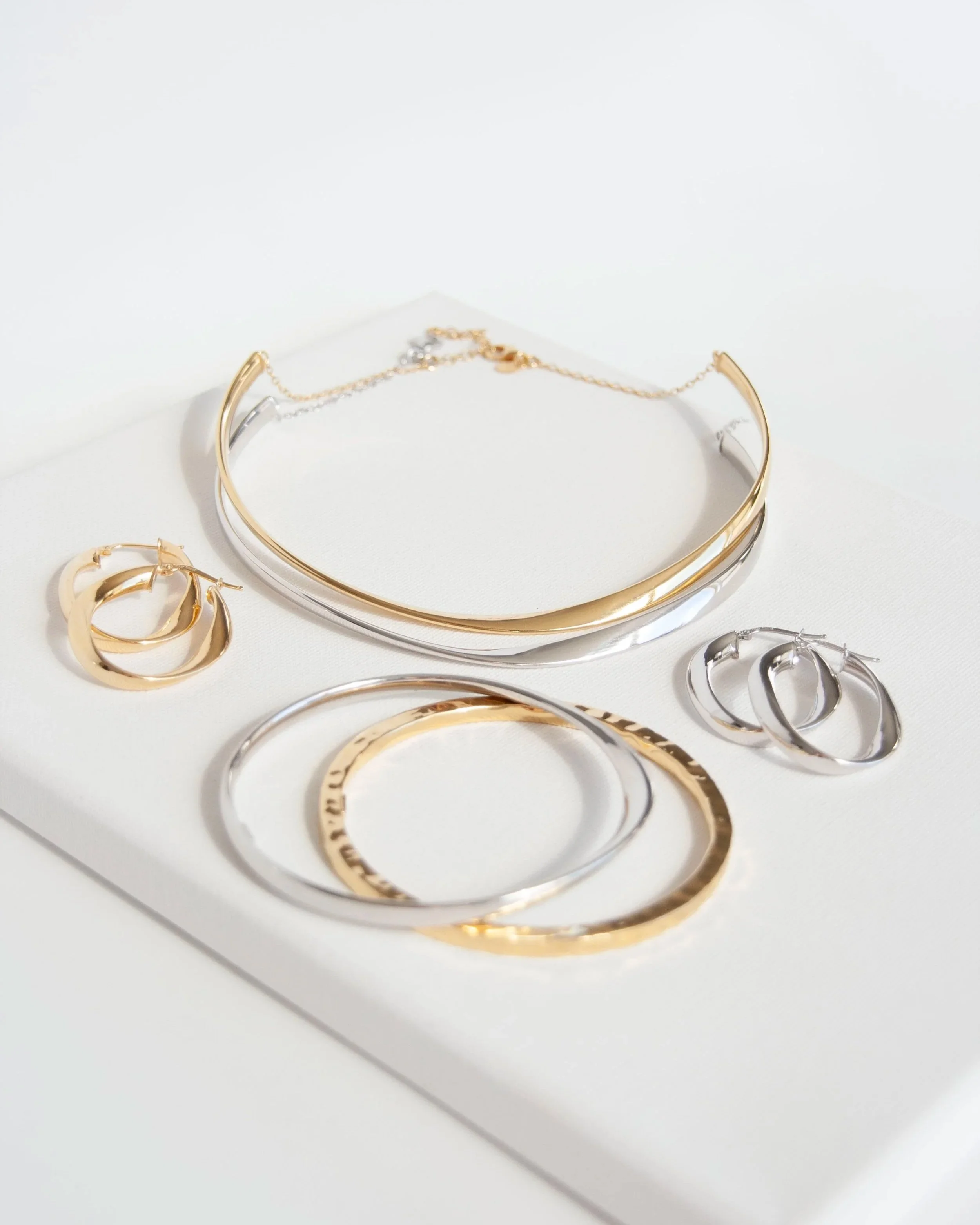 Gold and silver jewelry including necklaces, bracelets, and earrings displayed on a white surface.