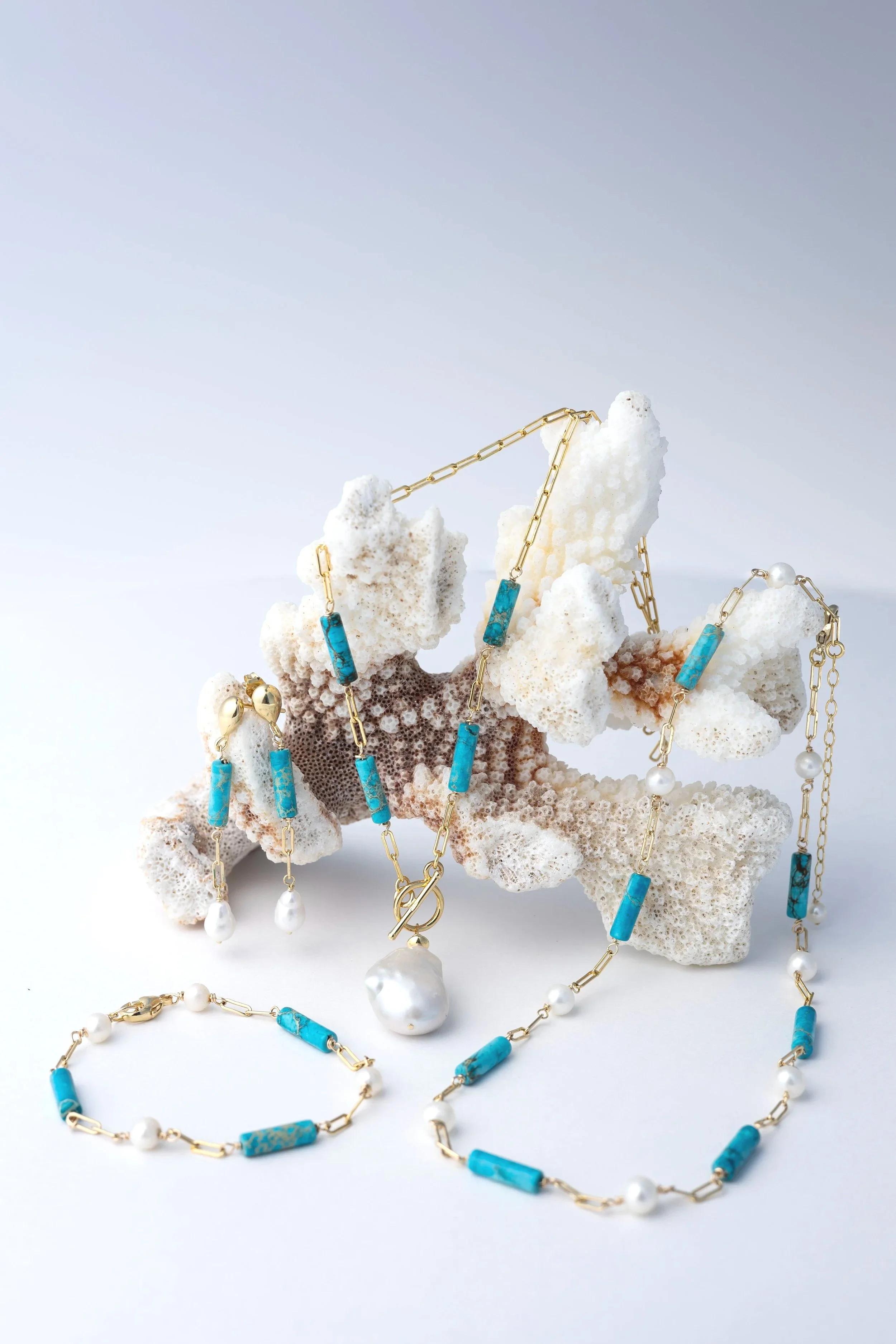 Jewelry including necklaces, earrings, and bracelets with blue stones and pearls, displayed on white coral.