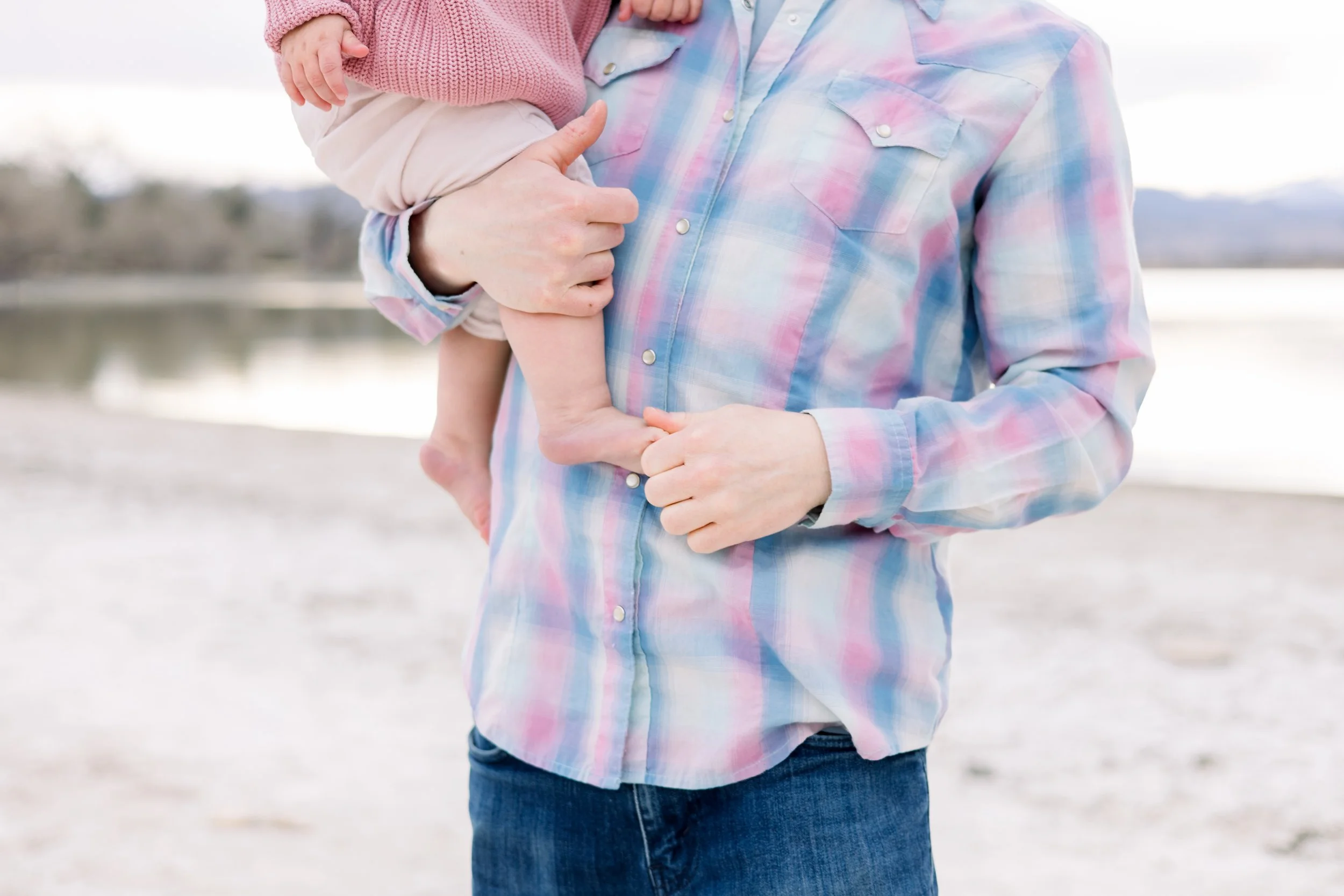 Person holding a child outdoors near a body of water, with both wearing casual clothing.