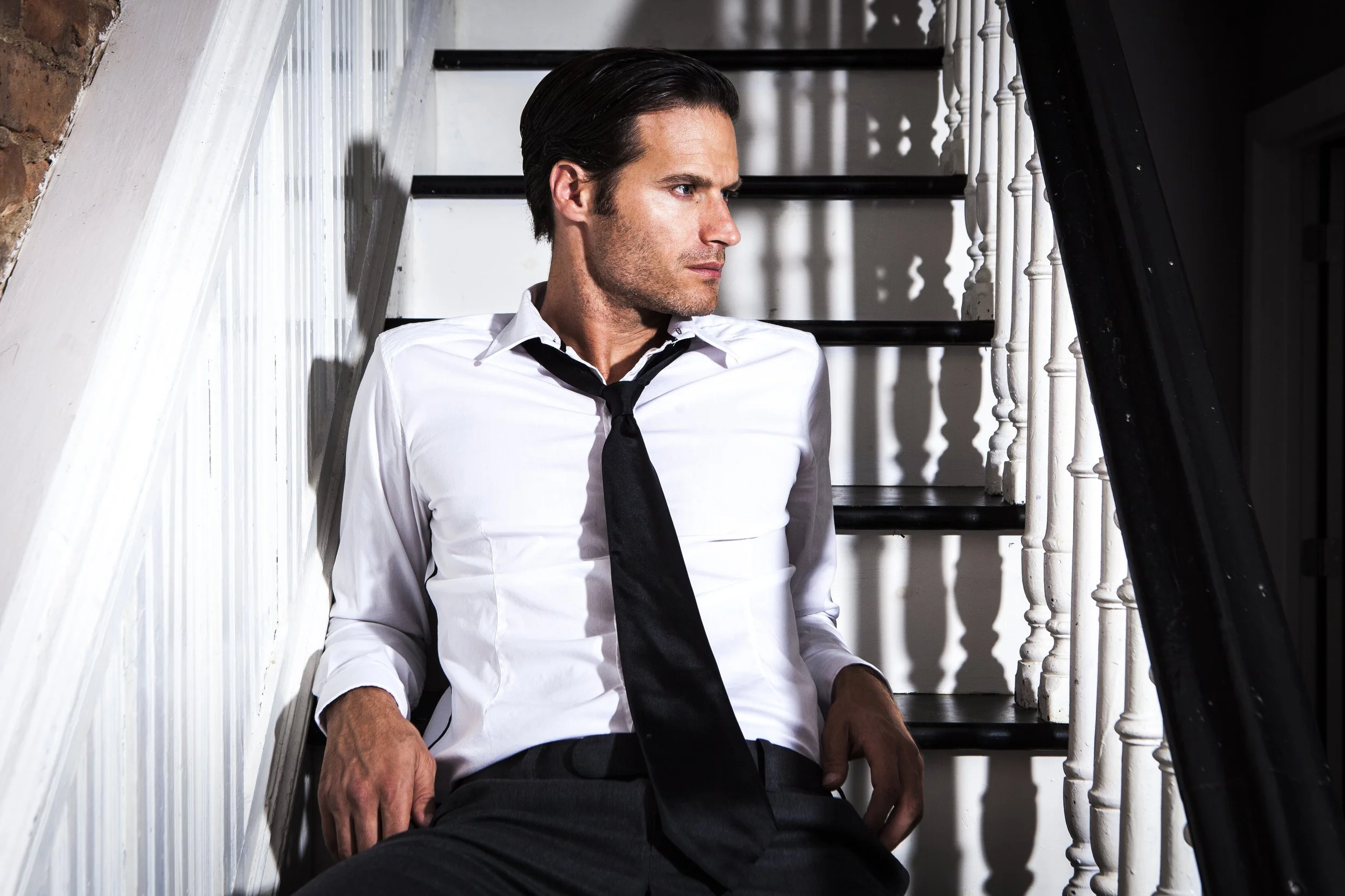 An editorial lifestyle portrait of the groom seated on a staircase, blending classic tailoring with a relaxed, modern sensibility.