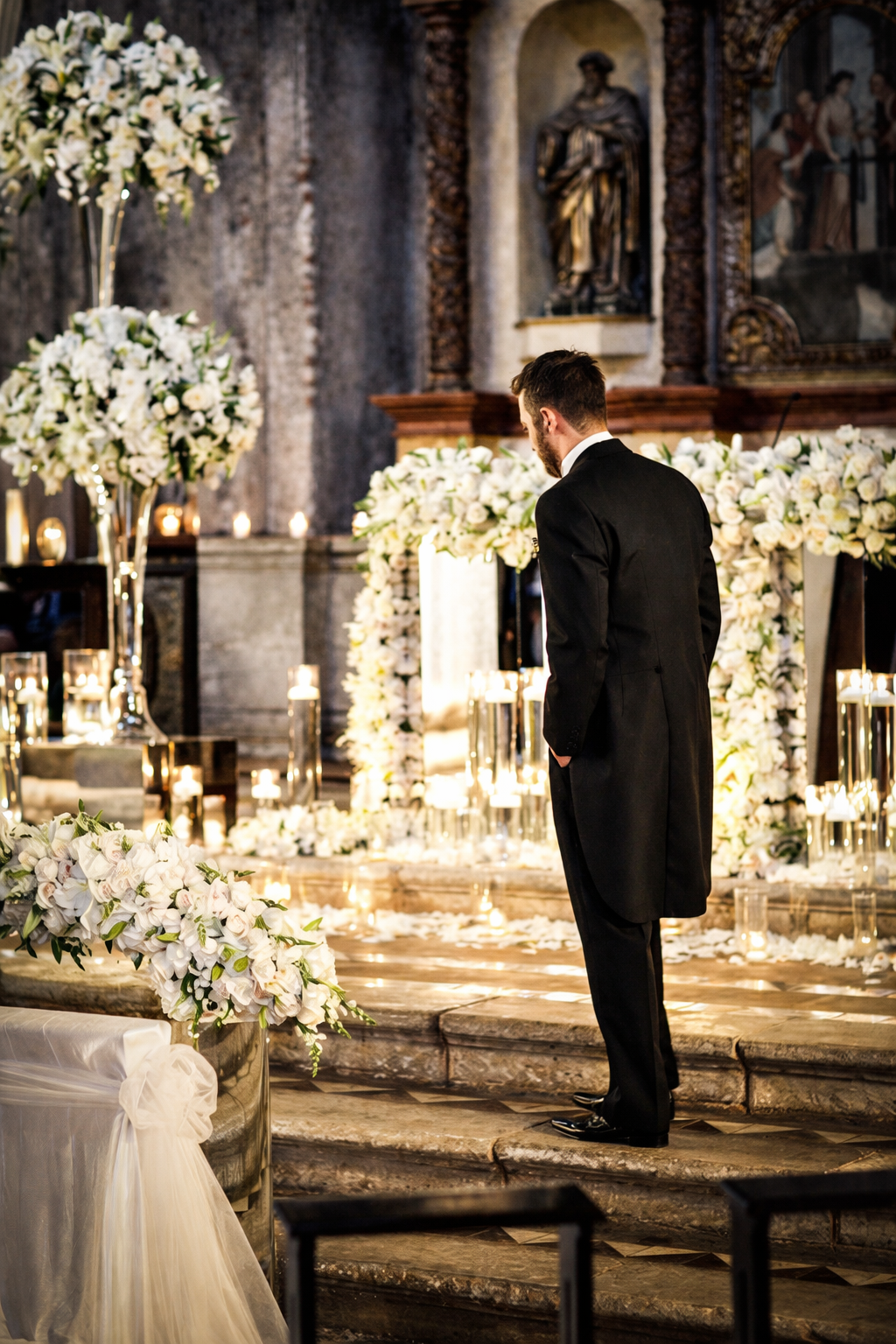 groom at altar, back turned, surrounded by florals + candles.