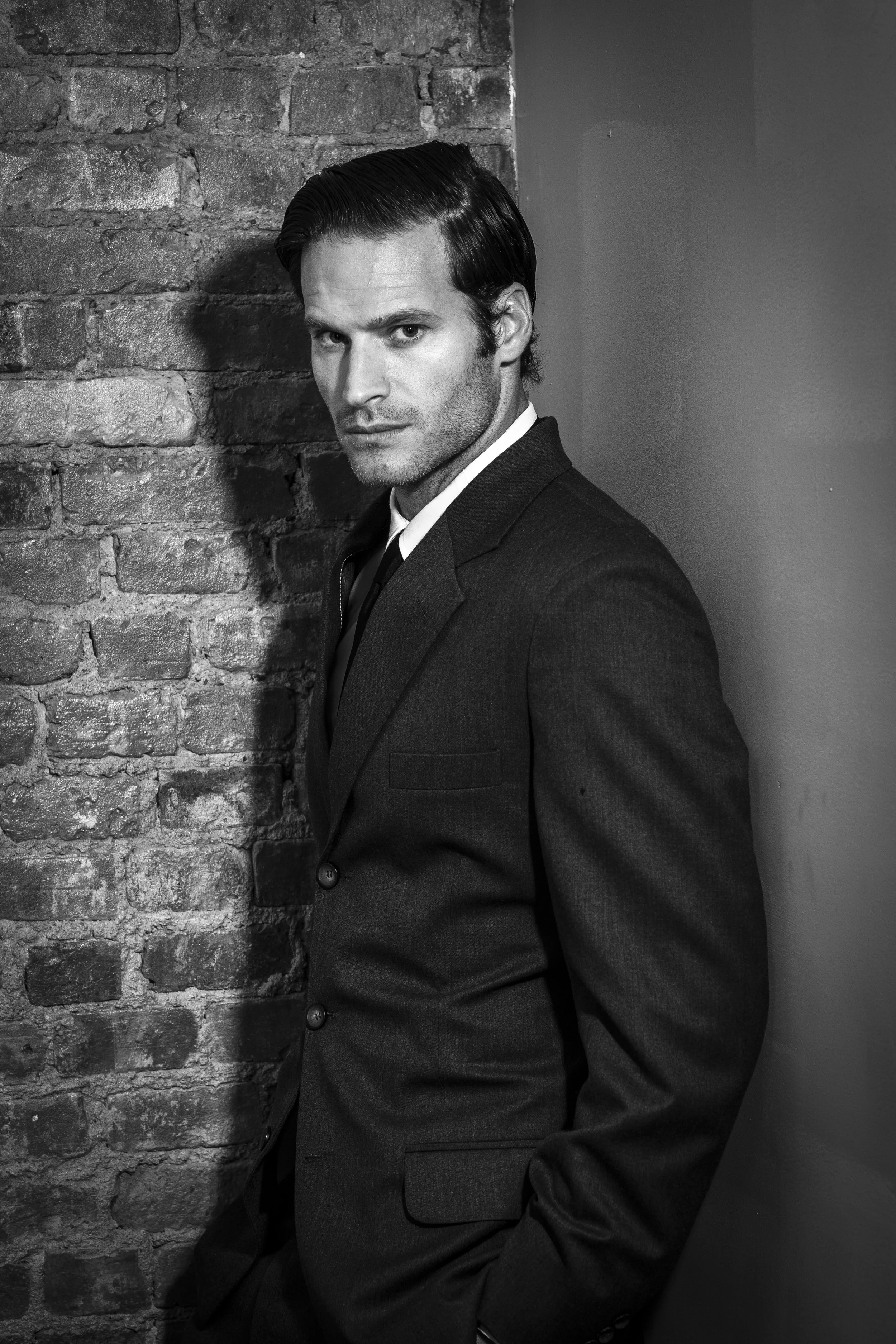 A cinematic black-and-white portrait of the groom, defined by strong lines, shadow, and a quietly confident editorial mood.