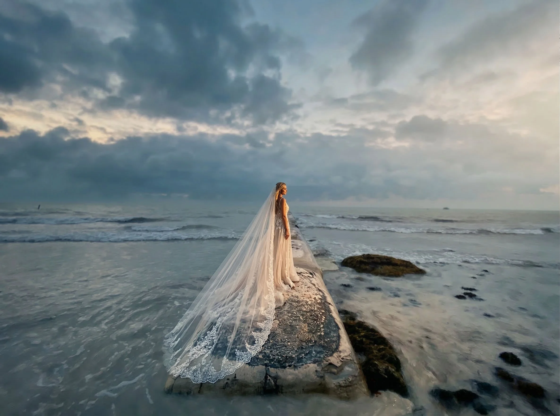 bride in flowing dress on ocean rocks with dramatic sky