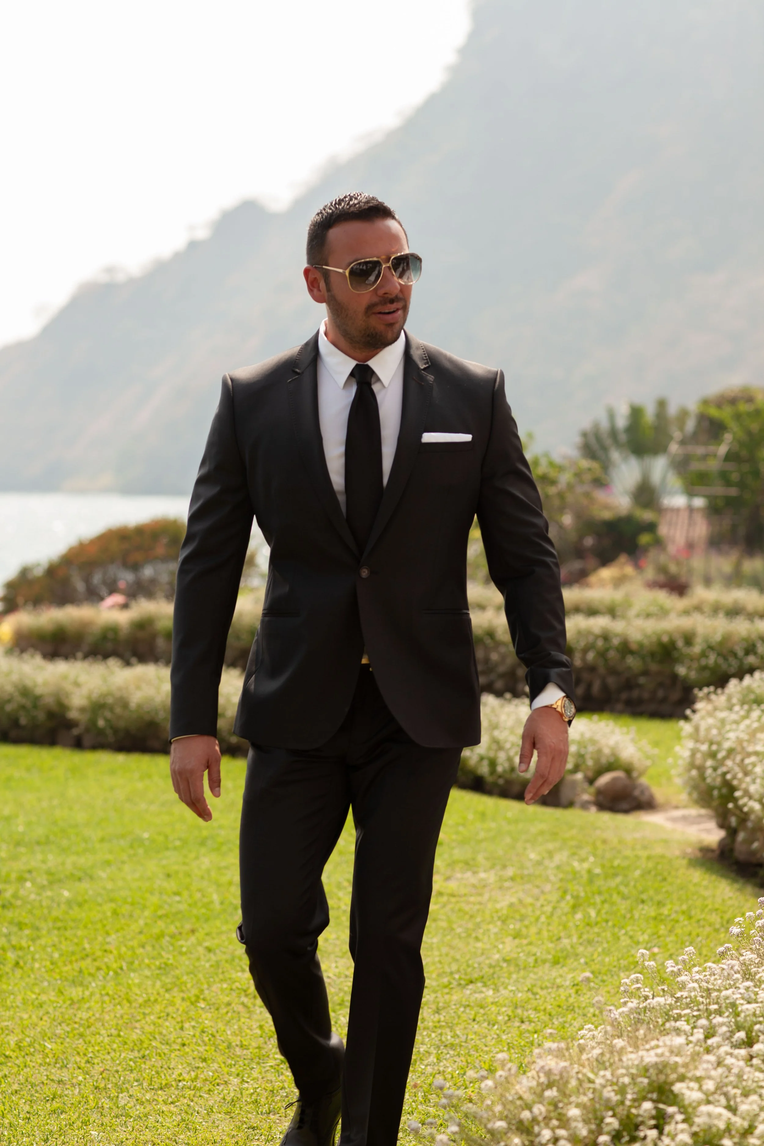 groom walking outdoors in black suit with mountains behind.