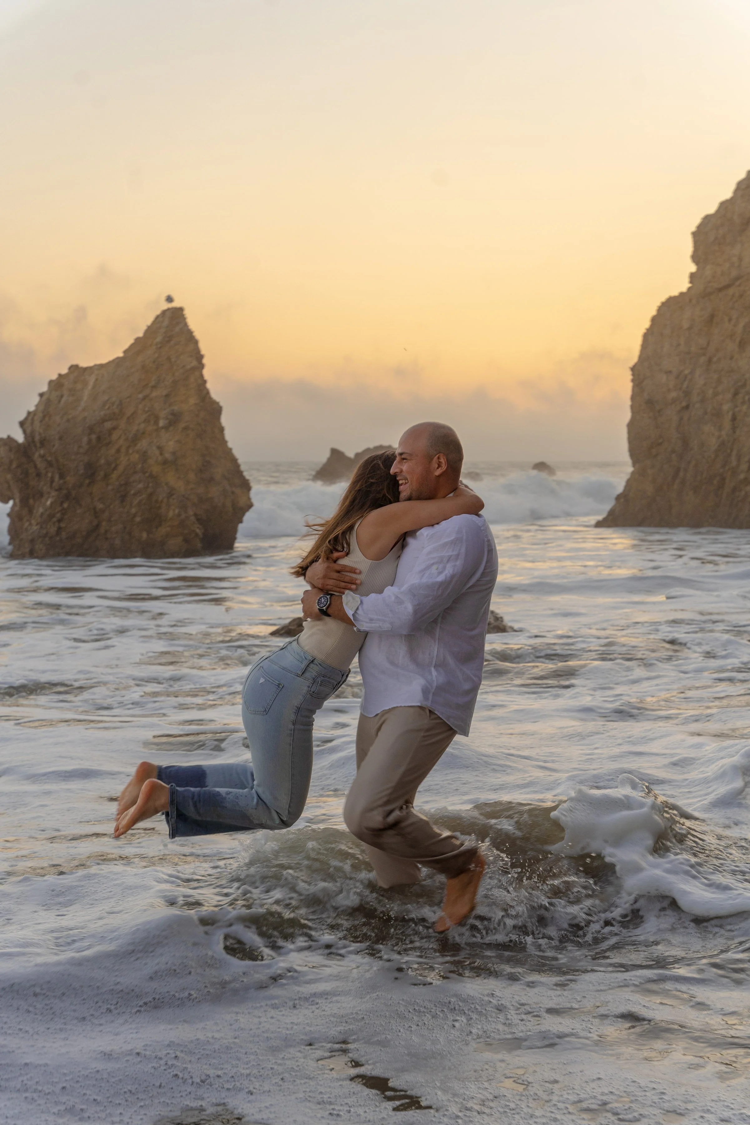 An organic moment of closeness as the couple celebrates together in the surf, surrounded by soft light and the rhythm of the ocean