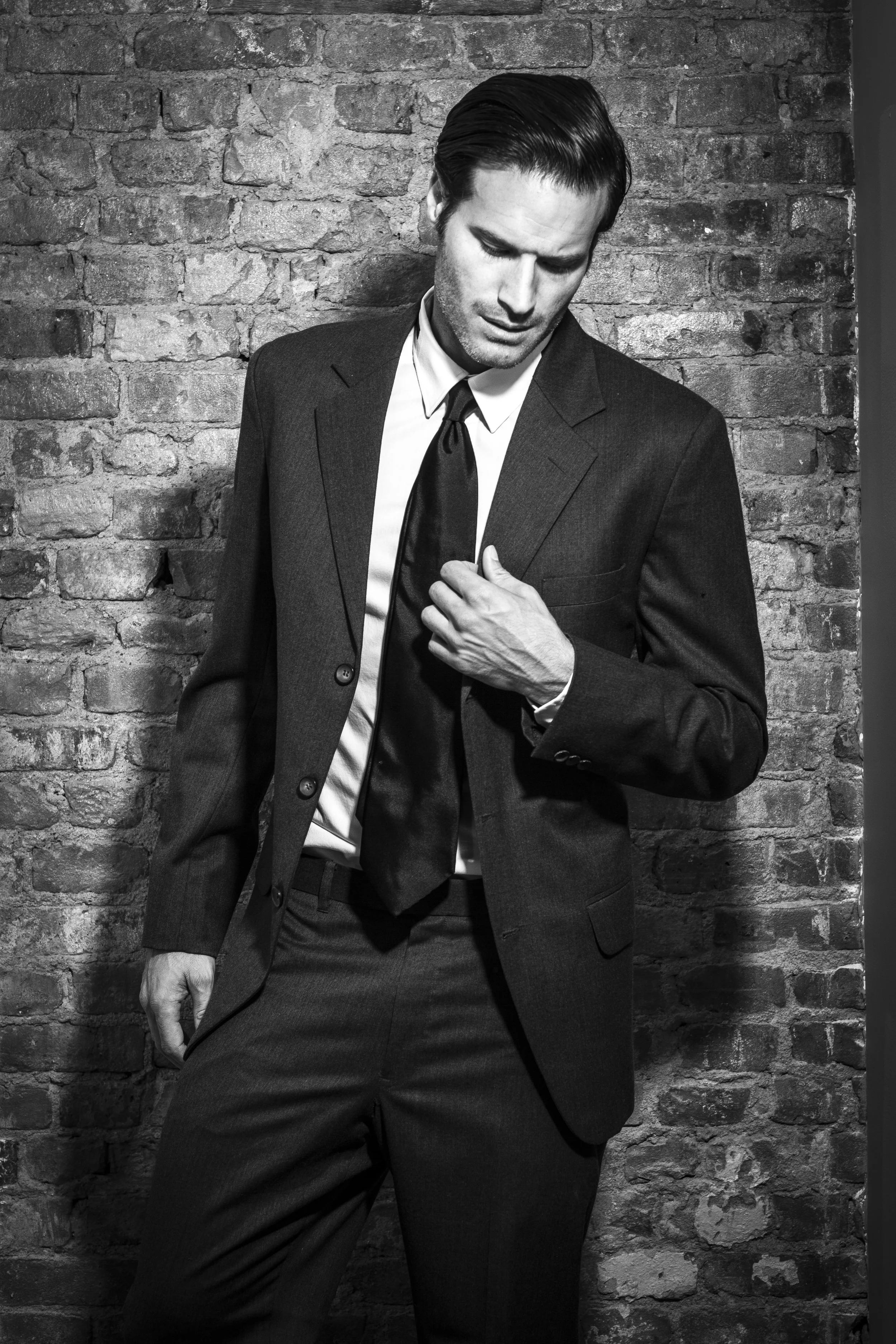 A refined black-and-white portrait capturing the groom adjusting his tie in a quiet pre-ceremony moment of anticipation and poise.