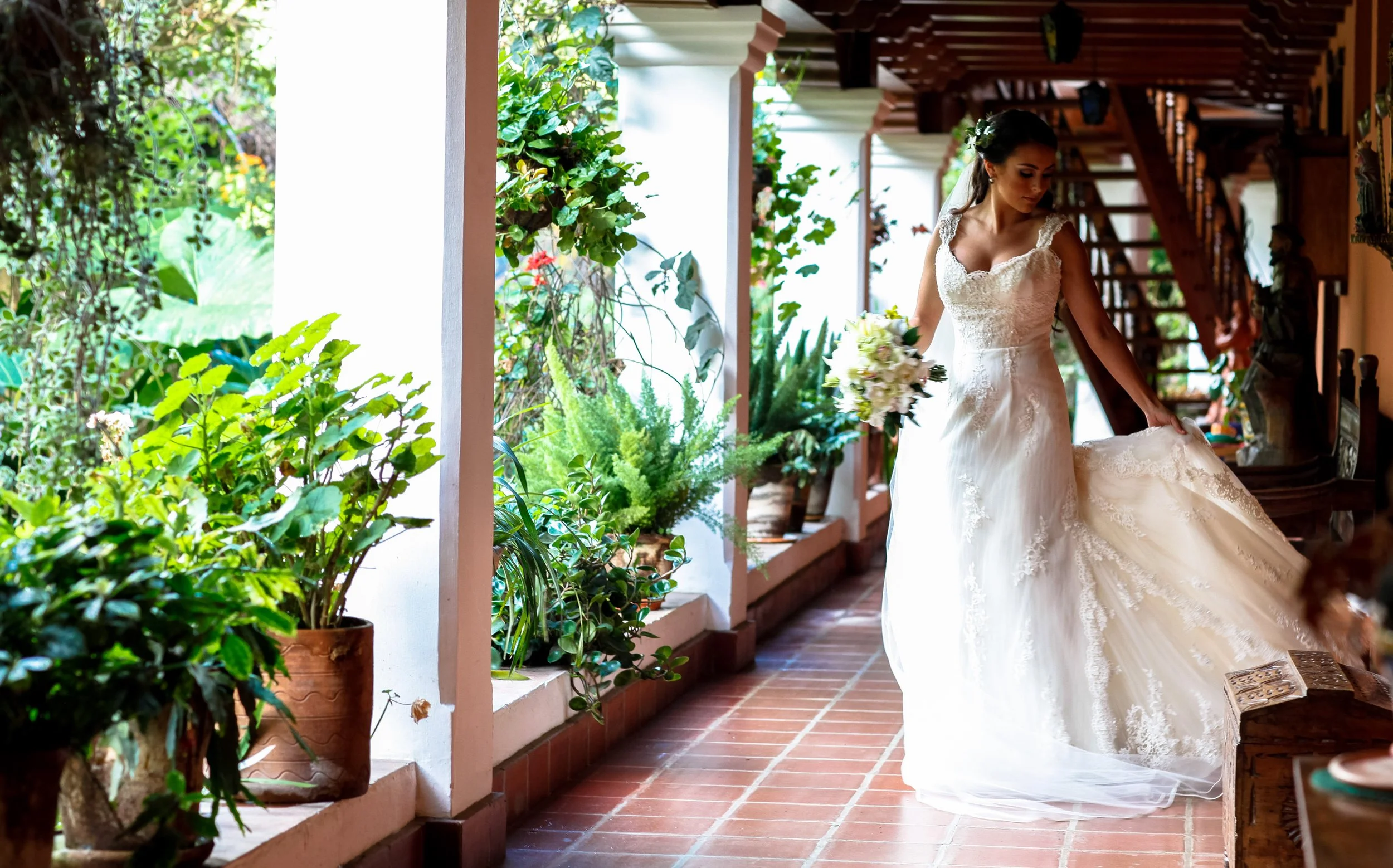 Flowing fabric trails behind the bride as she walks through a sunlit corridor, combining movement with architectural warmth.