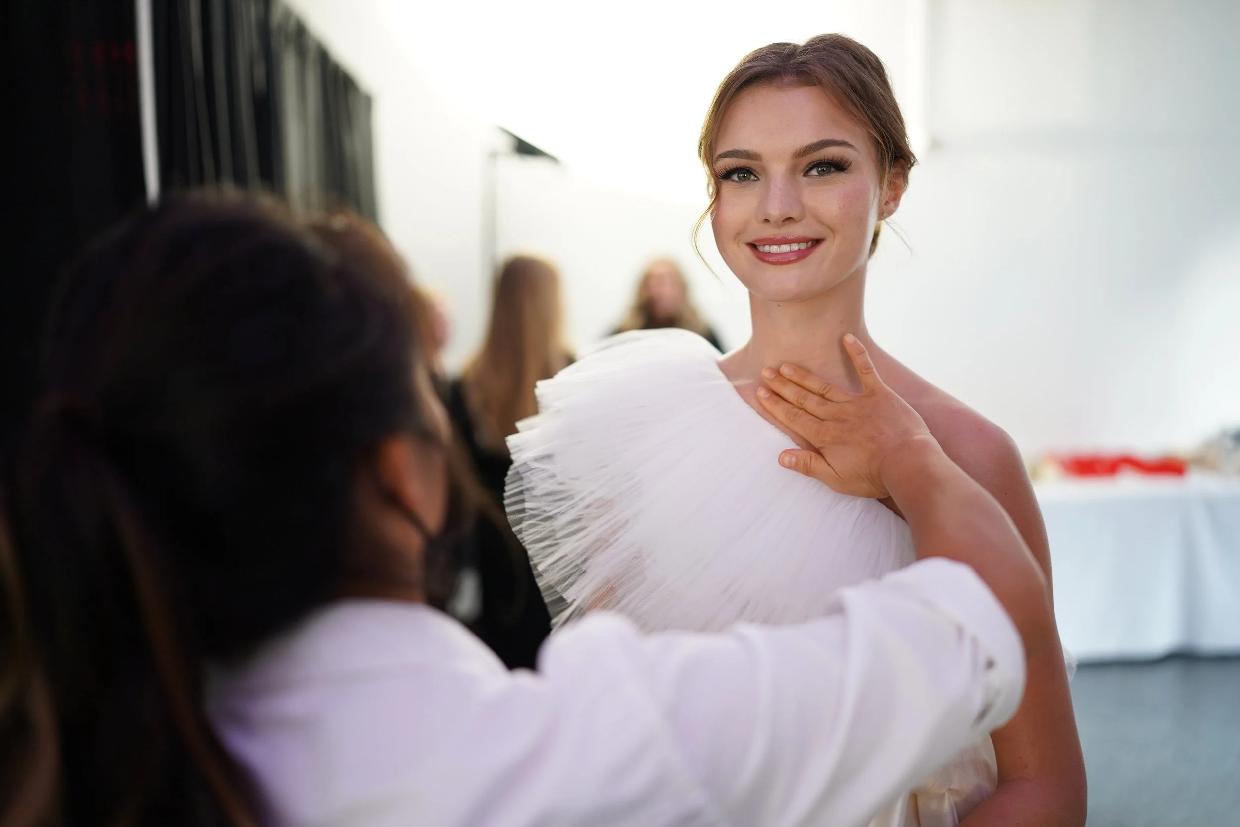 stylist touching the neckline / chest area of the one-shoulder short dress, bride facing camera