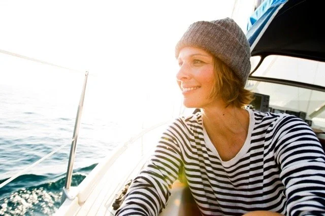 Eine junge Frau mit gestrickter Mütze und gestreiftem Hemd sitzt auf einem Boot und genießt die Aussicht auf das Meer bei Sonnenaufgang oder Sonnenuntergang.