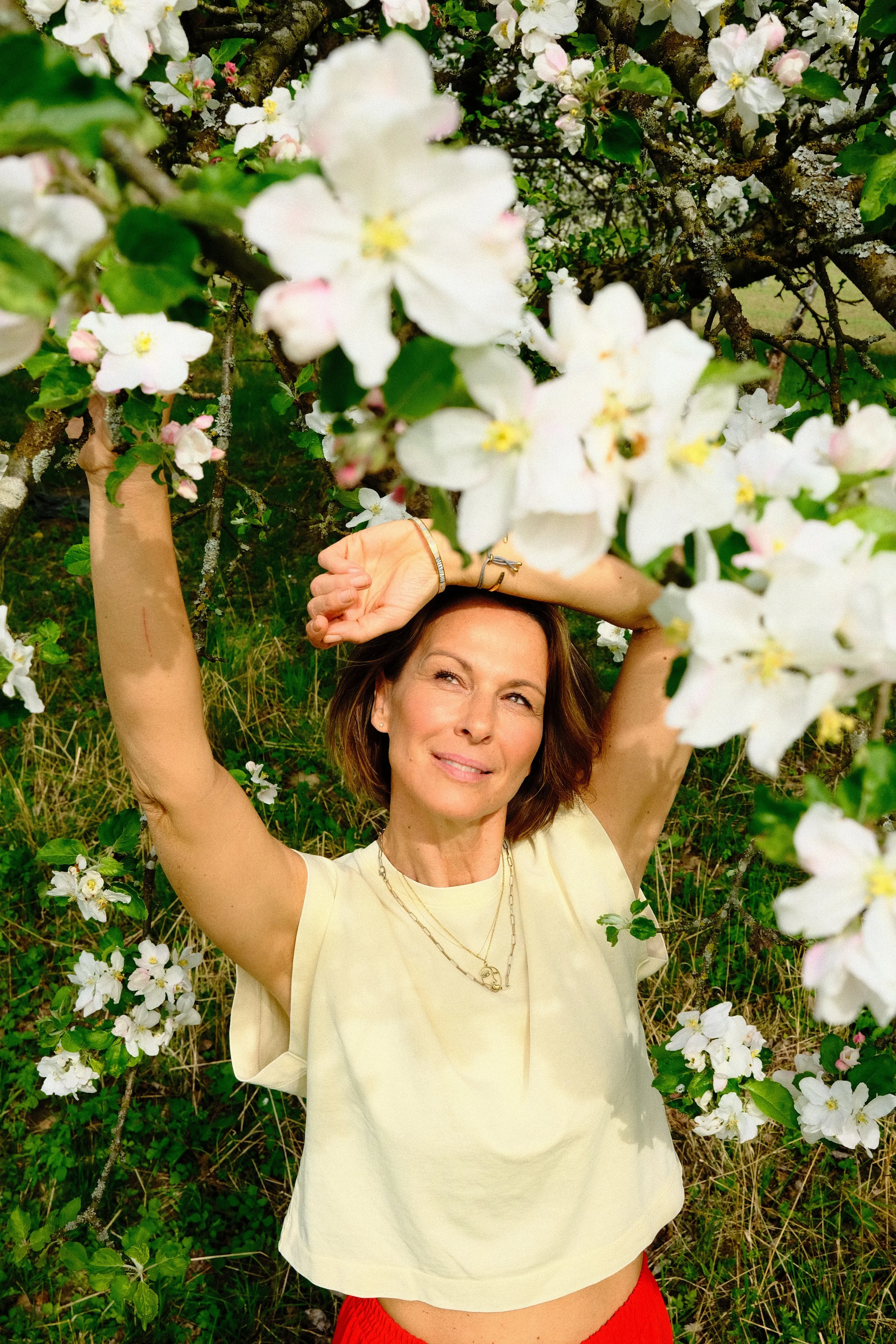 Frau mit braunen Haaren und rotem Rock steht unter Kirschblüten und posiert nervös.