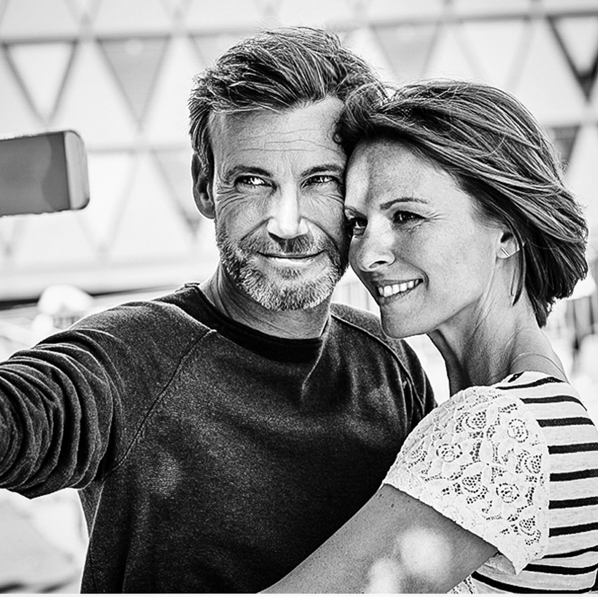 zwei Menschen, ein Mann und eine Frau, beim Posieren für ein Selfie, lächelnd, im Freien, schwarz-weiß.