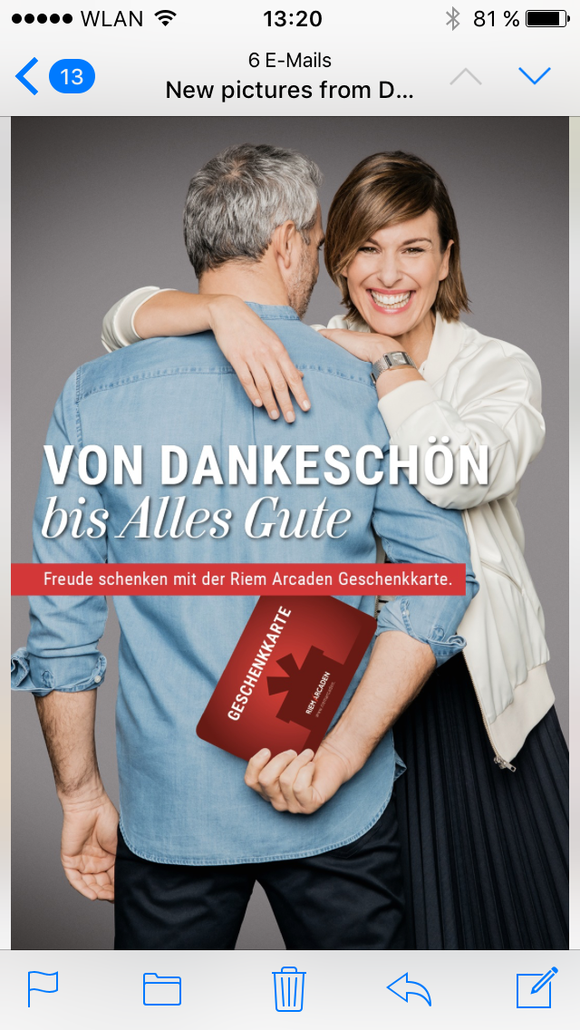 Ein lachendes Paar umarmt sich, eine Frau gibt einem Mann einen Kuss auf die Wange. Der Mann hält eine rote Geschenkkarte. Der Hintergrund ist grau, und der Text auf dem Bild lautet "VON DANKESCHÖN bis Alles Gute". Es wird eine Gutscheinkarte der Rie