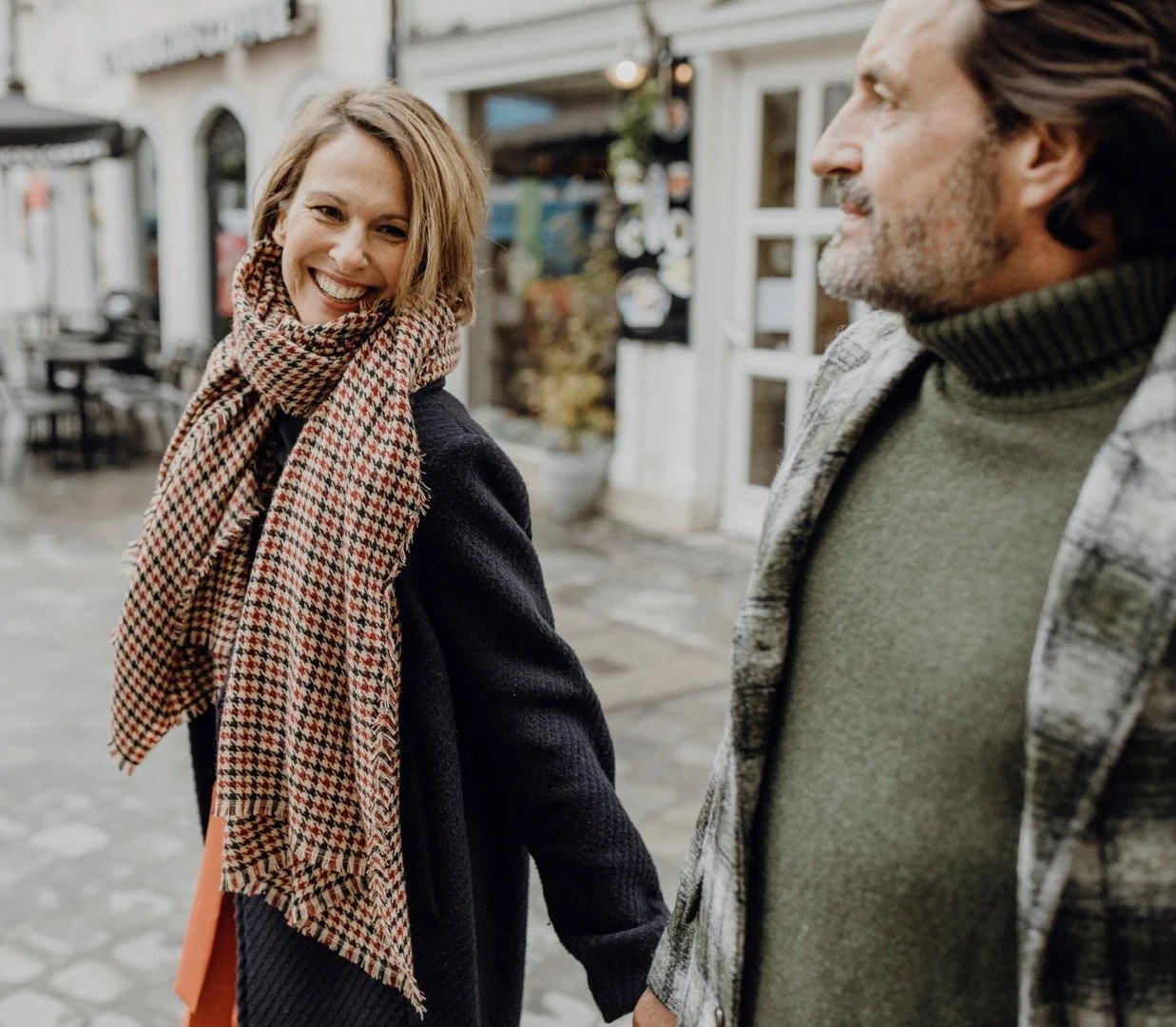 Ein lachendes junges Mädchen, das einen Kuss gibt, während ein älterer Mann daneben steht, in einer Straßenumgebung vor Geschäften.