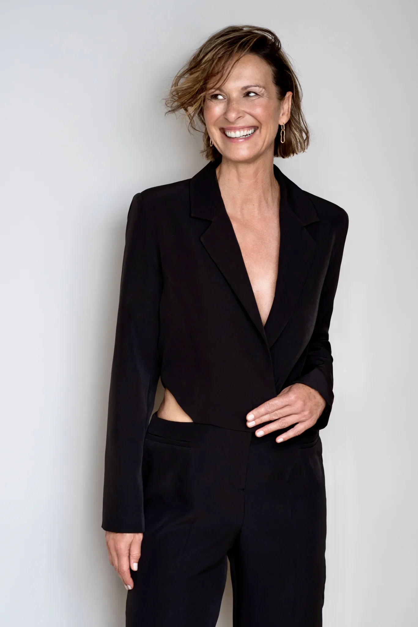 Eine lachende Frau in einem schwarzen Anzug vor einem weißen Hintergrund.