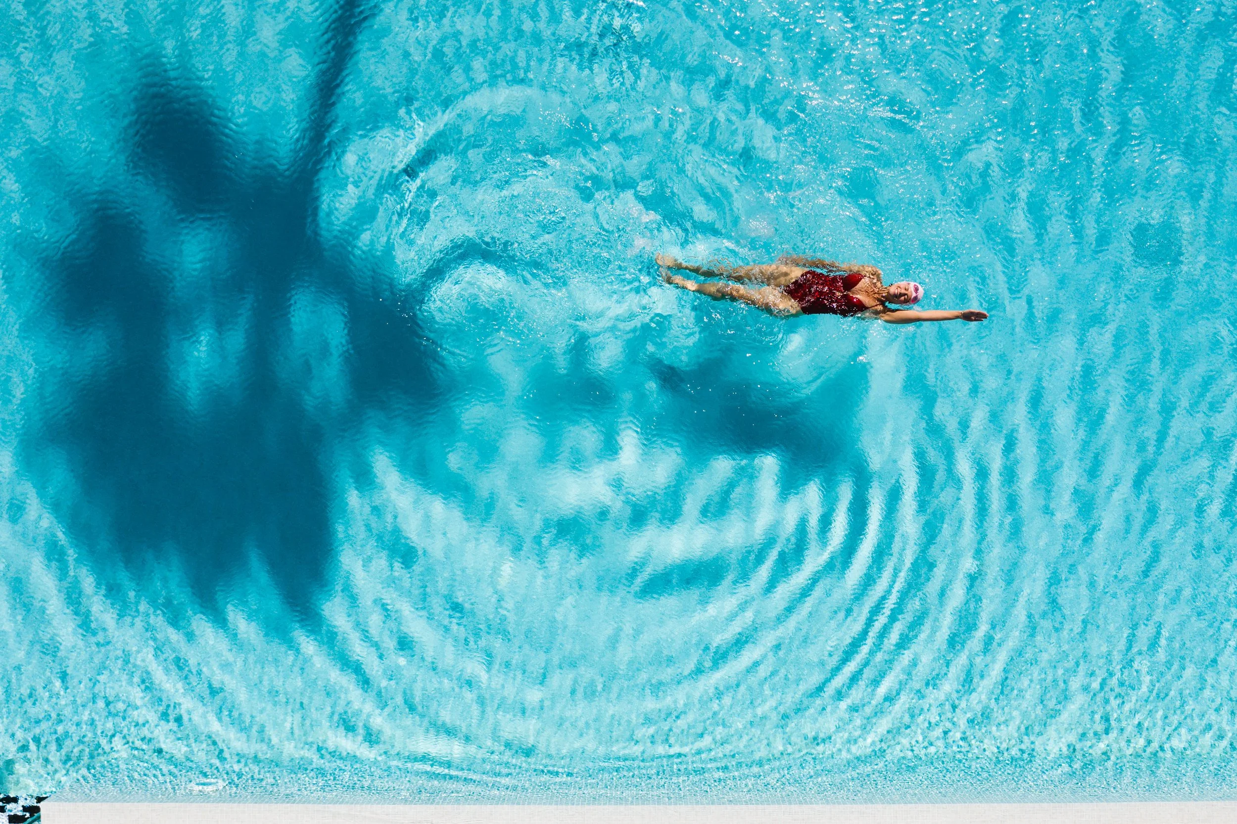 Eine Schwimmerin in einem Schwimmbad, die gerade einen Schwimmzug macht, trägt eine rote Badebekleidung und eine pinke Badekappe.