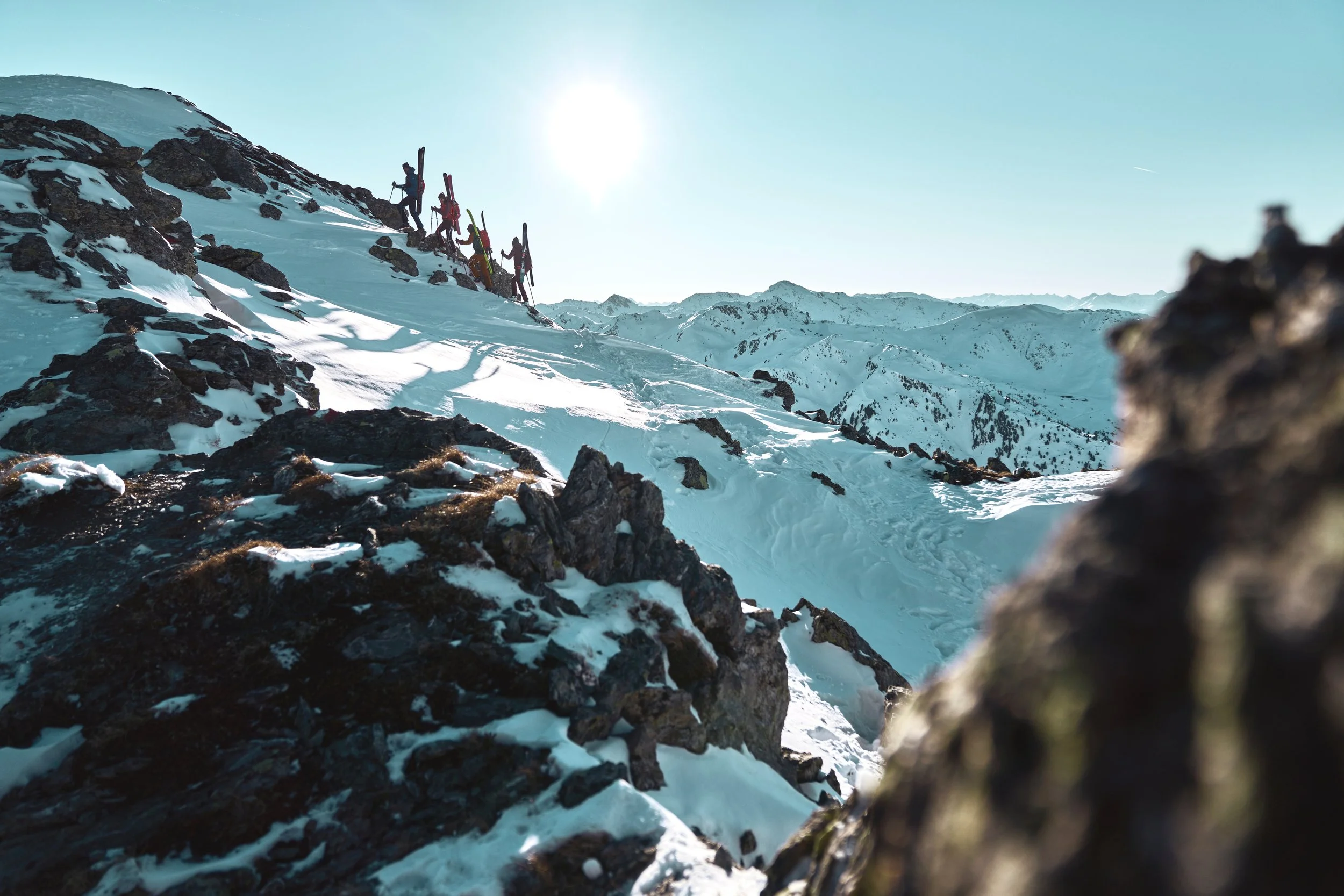 Gruppe von Skifahrern auf verschneitem Bergpfad im Hochgebirge bei sonnigem Himmel.