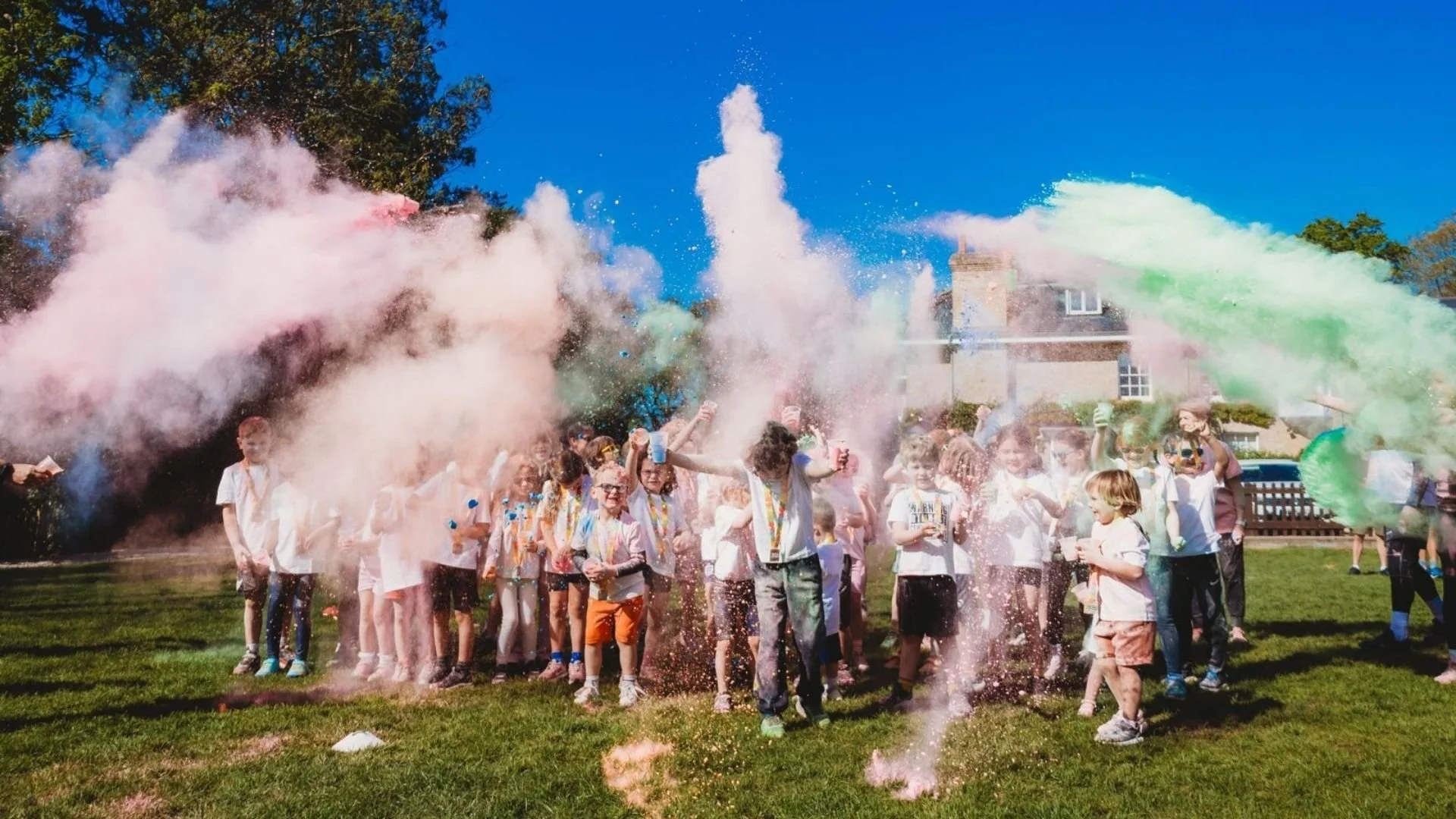Children celebrating outdoors with colorful powder being thrown in the air during daytime.
