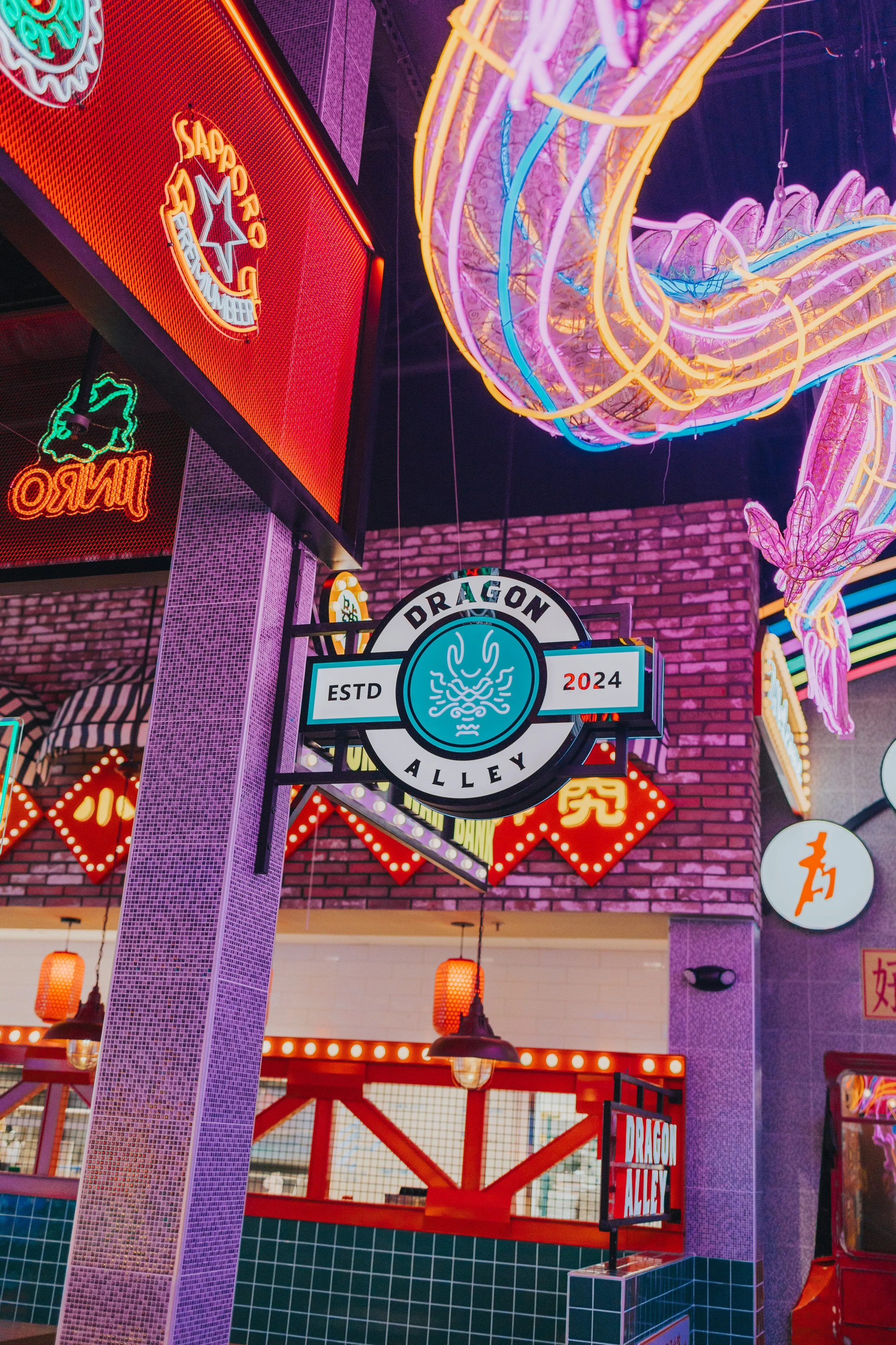 Neon signs and decorative lighting at Dragon Alley, established in 2024, with various vibrant neon signs, including a dragon logo, Chinese characters, and other colorful lights in an indoor entertainment or dining area.