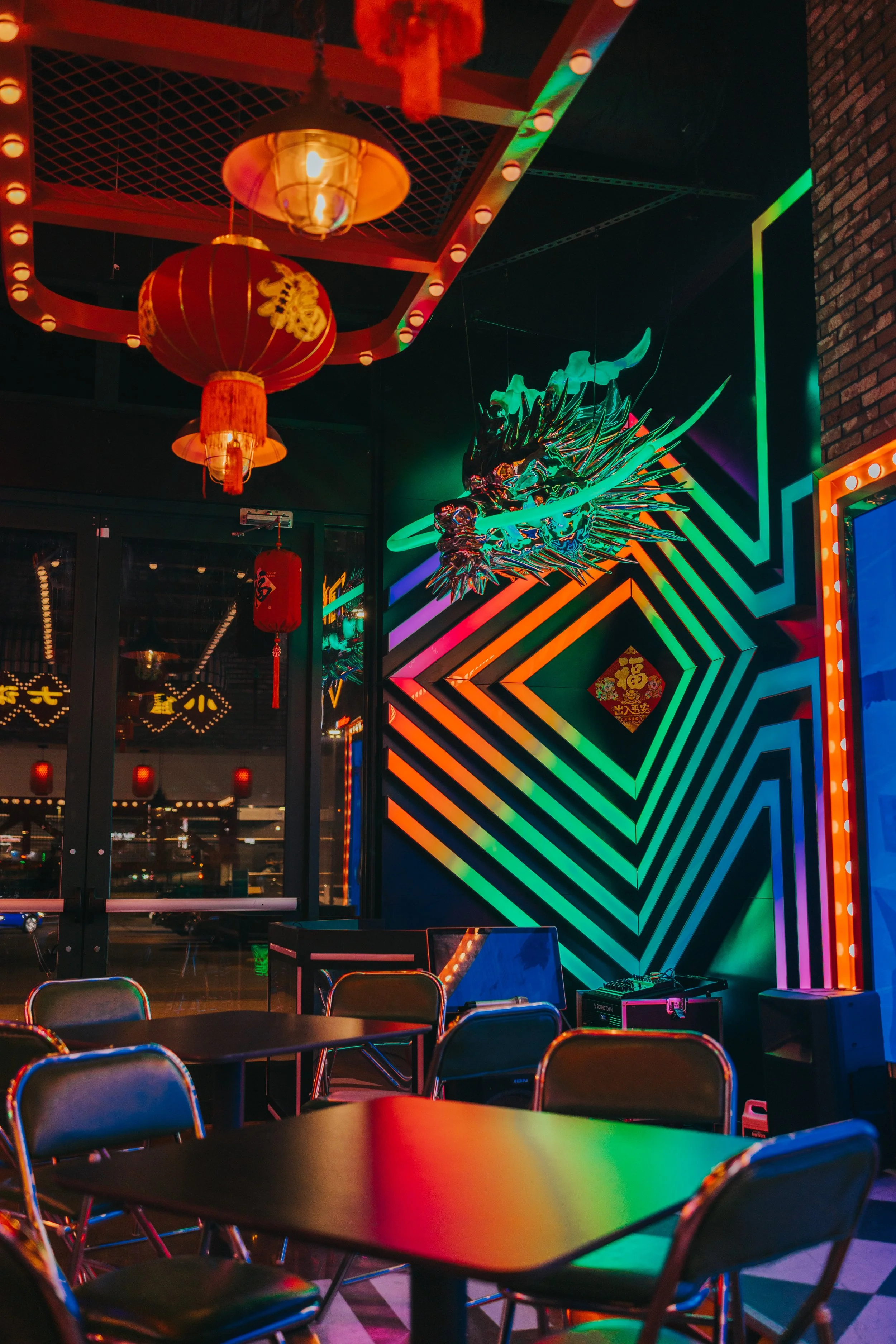 Interior of a vibrant restaurant decorated with Chinese lanterns and neon-lit dragon art, with tables and chairs arranged for dining.