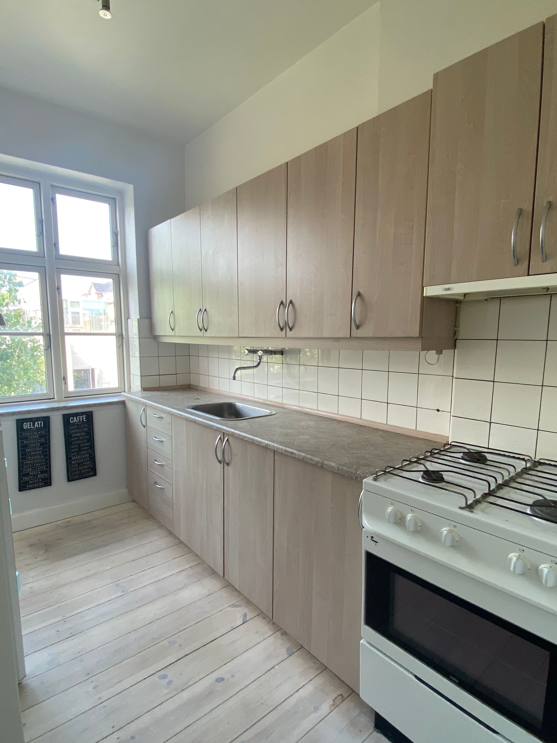 Kitchen with light wood cabinets, white tiled backsplash, a small sink under a window, and a white gas stove.