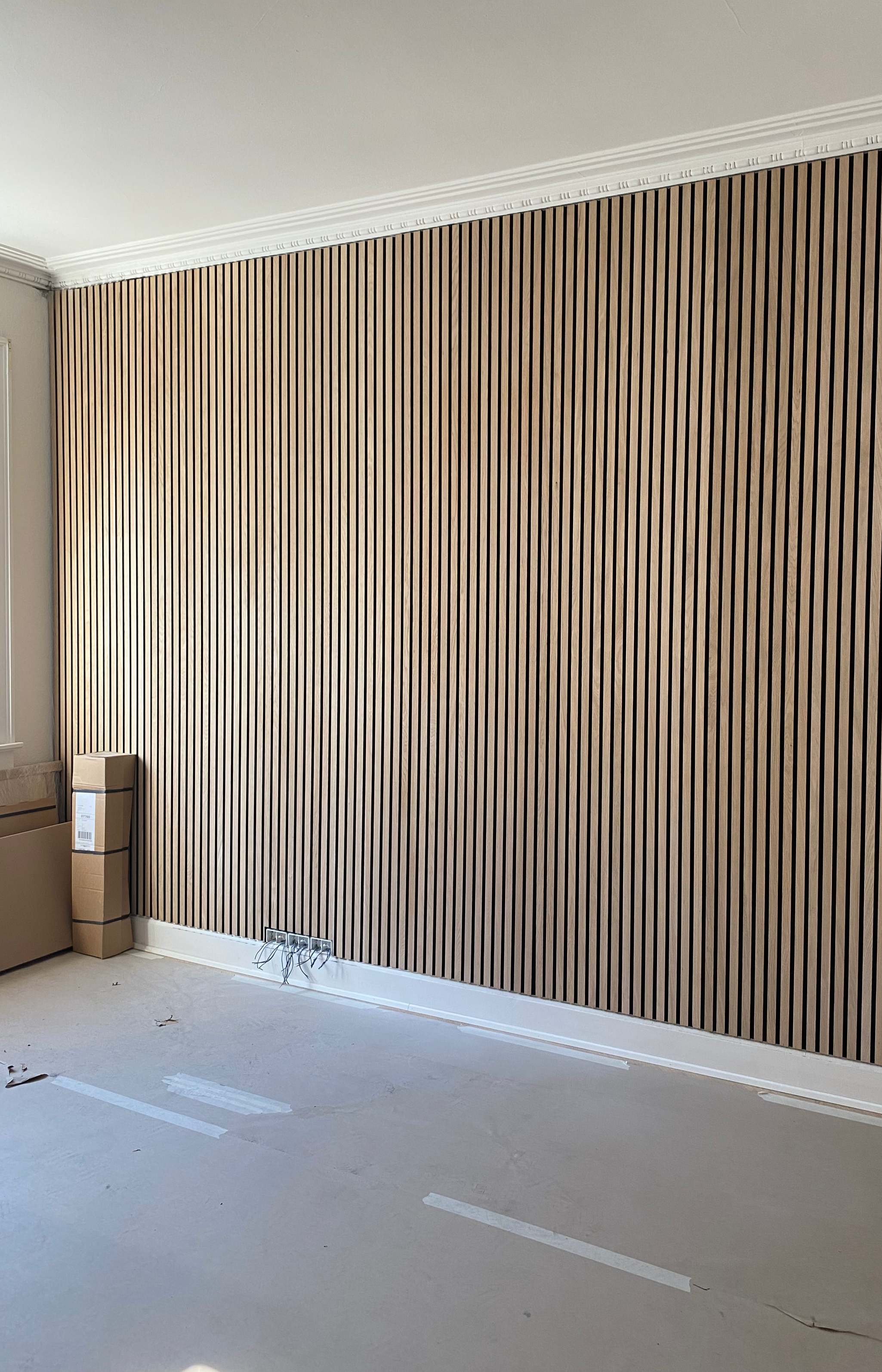 Interior room with a wood-paneled accent wall, electrical outlets and wiring near the baseboard, cardboard boxes on the floor, and light-colored flooring.