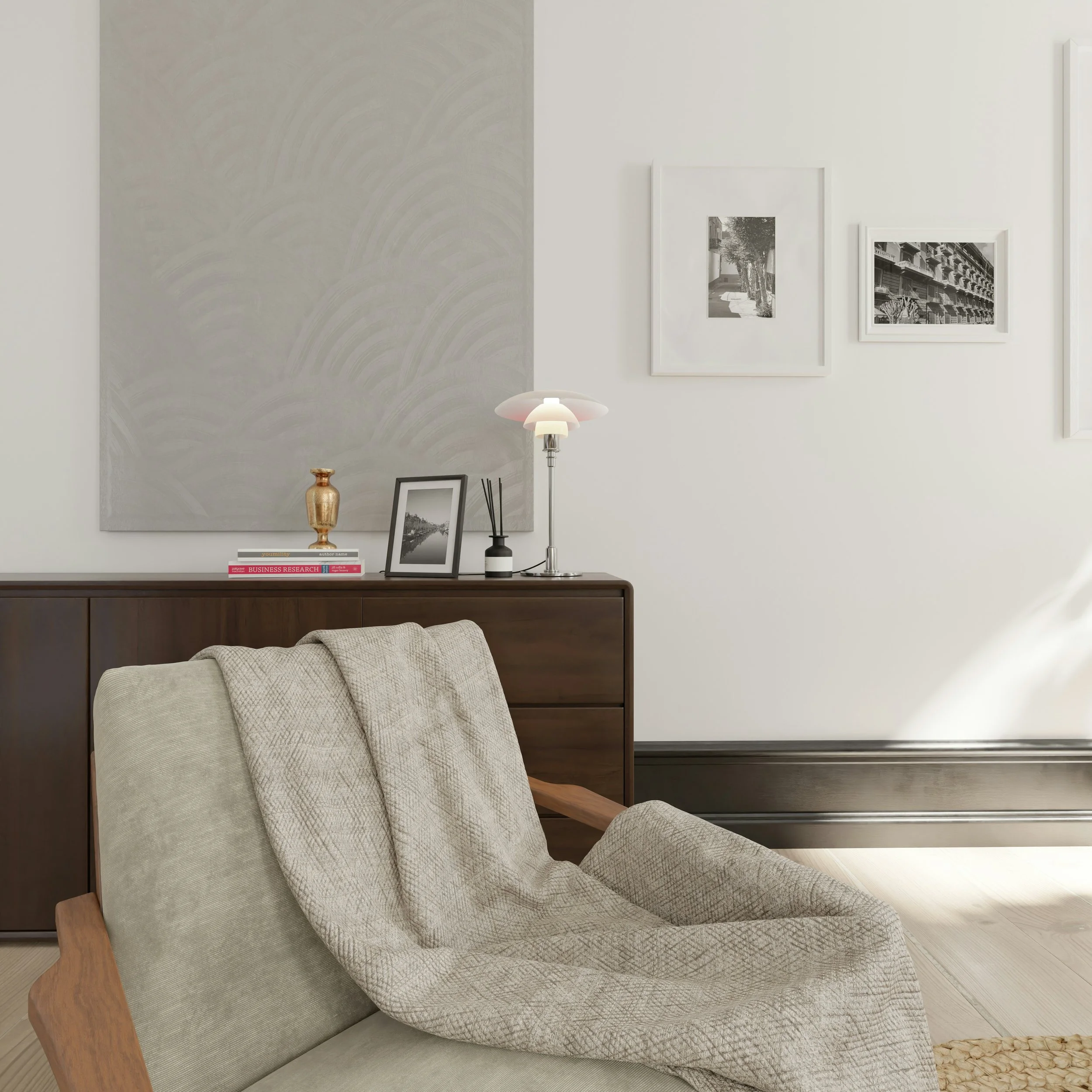 A beige armchair with a textured throw blanket in a contemporary living room with a wooden sideboard, black and white framed photo, gold decorative vase, small black and white diffuser, and a modern table lamp with a pink and white shade.