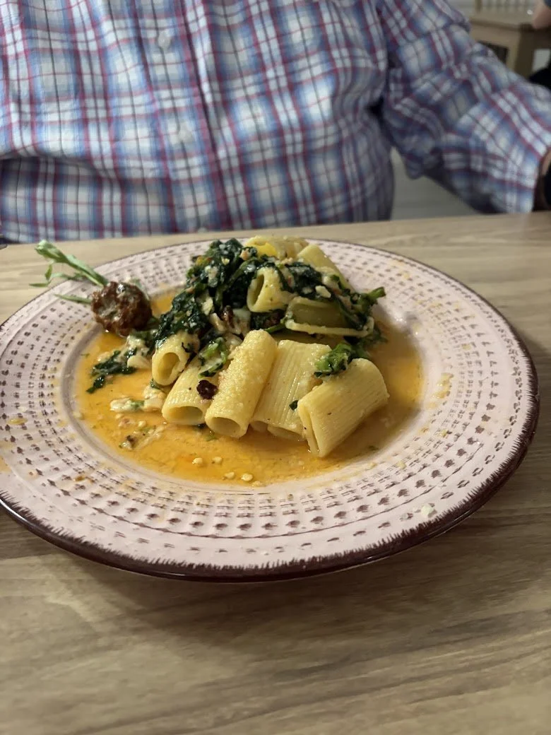 Plate of pasta with spinach and a creamy sauce on a wooden table, person wearing a plaid shirt in the background.