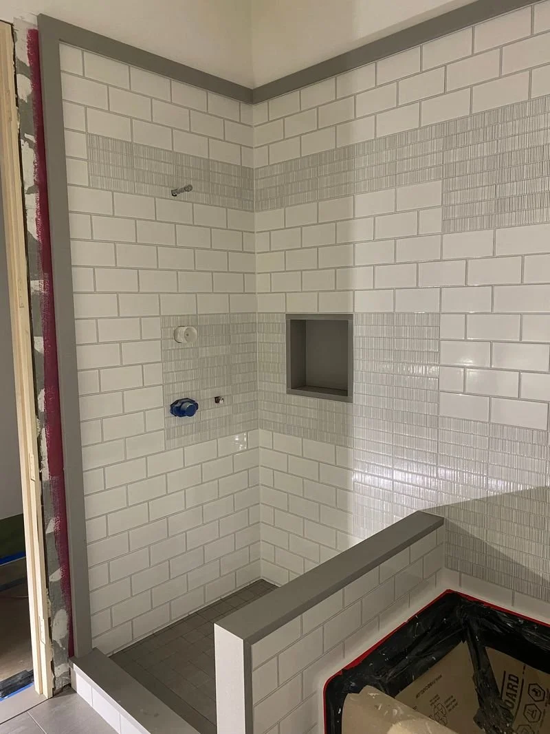 Bathroom shower area under construction with white subway tiles, a built-in niche, and partial framing for a glass door.