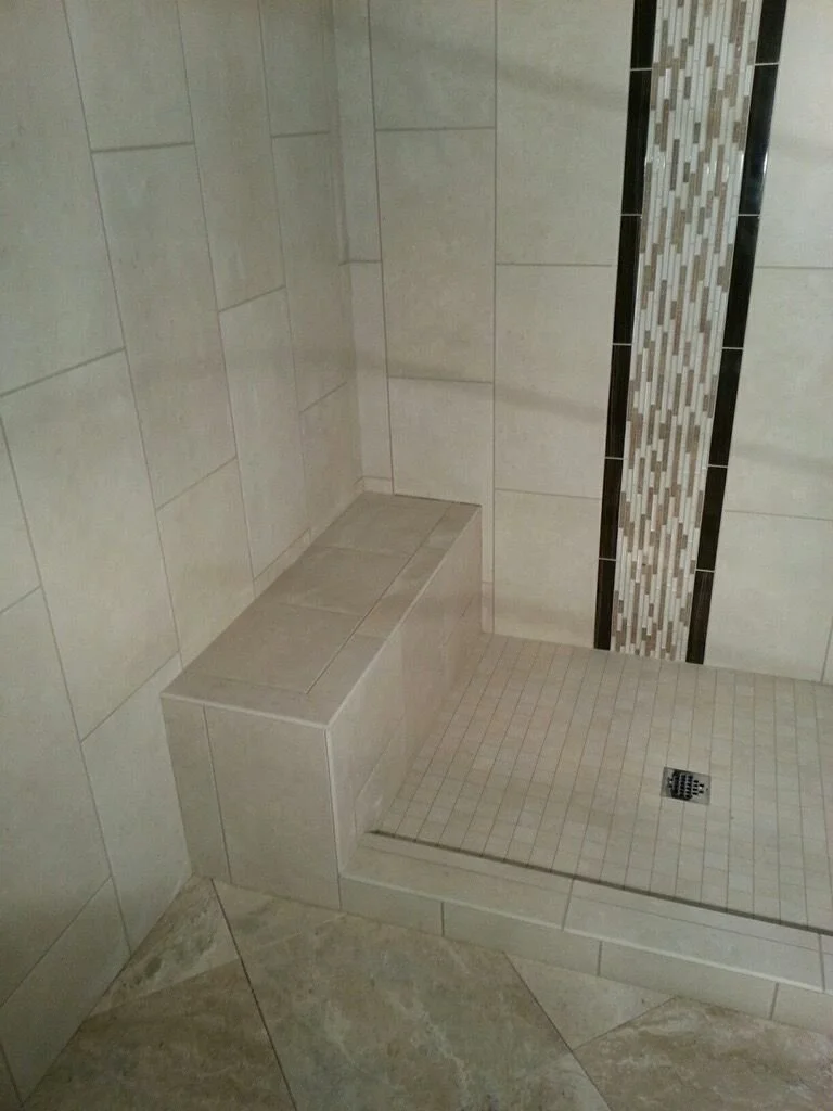 A tiled shower with a built-in seat, a central drain, and decorative mosaic vertical strip on the wall.
